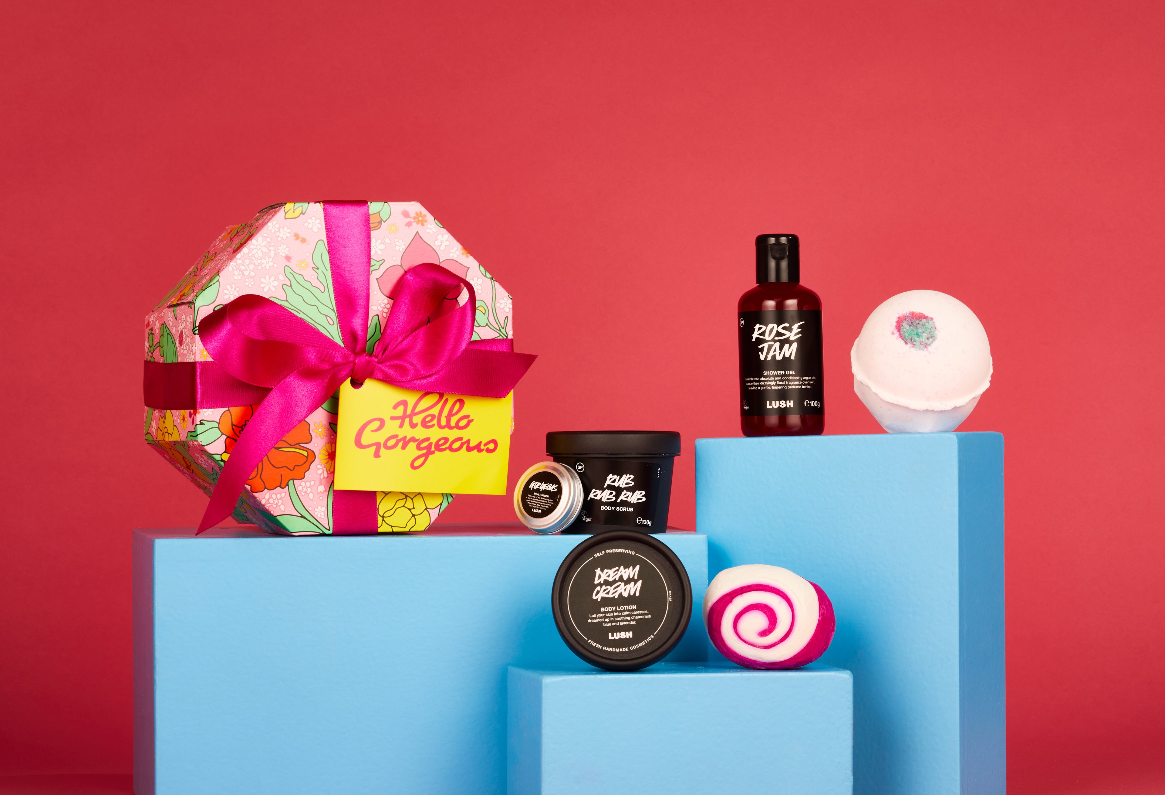 Gift products are displayed on tiered blue blocks with the gift box on the left on a deep red background.