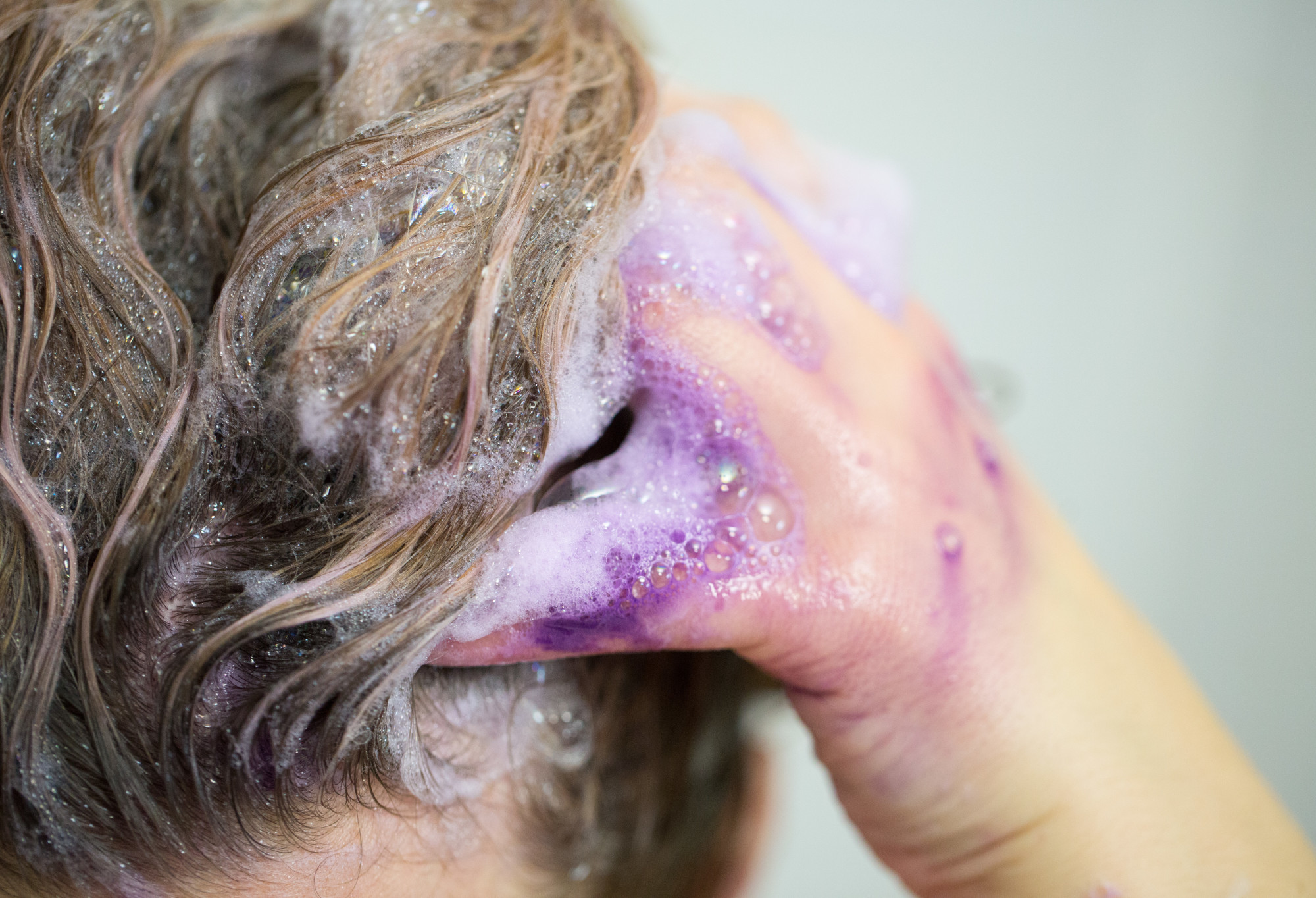 Someone massages vibrant purple Daddy-O shampoo into the back of their head, creating a mass of lilac coloured bubbles.