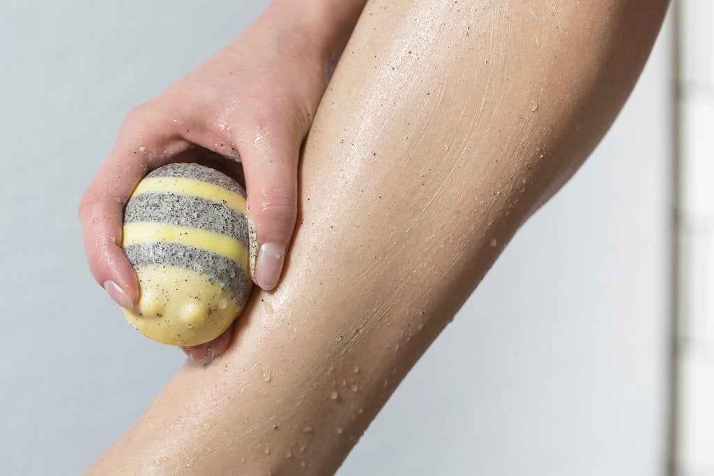 Scrubee, a cream, bee shaped body butter, is being swept over a water beaded leg.