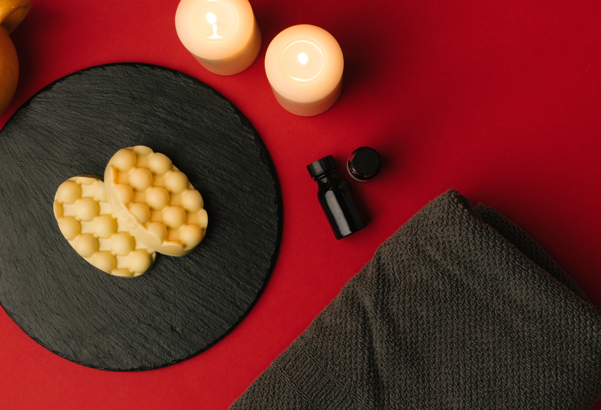2 yellow, oval shaped Hottie massage bars are presented on a circular slate, accompanied by warm candles, oils and a grey towel.