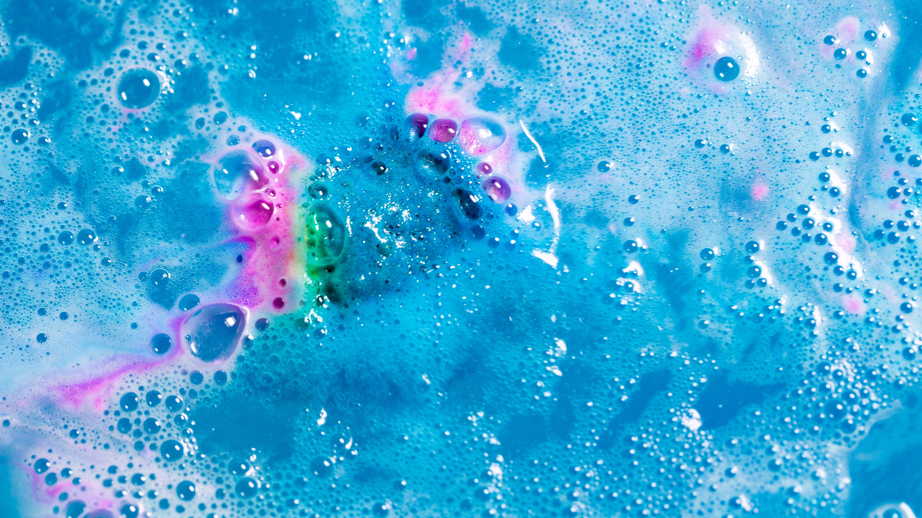 Bright blue, pink and white foam sit atop dark waters, creating a deep space effect. A myriad of bubbles complete this galaxy.