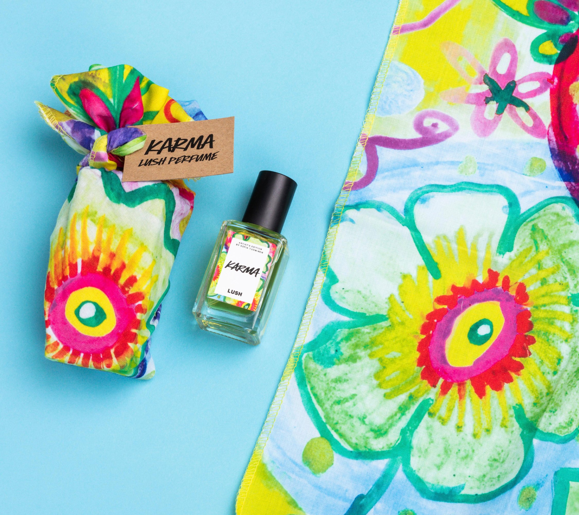 Karma lies on a light blue background, alongside its two elements: a small bottle of Karma perfume and a colourful knot wrap.