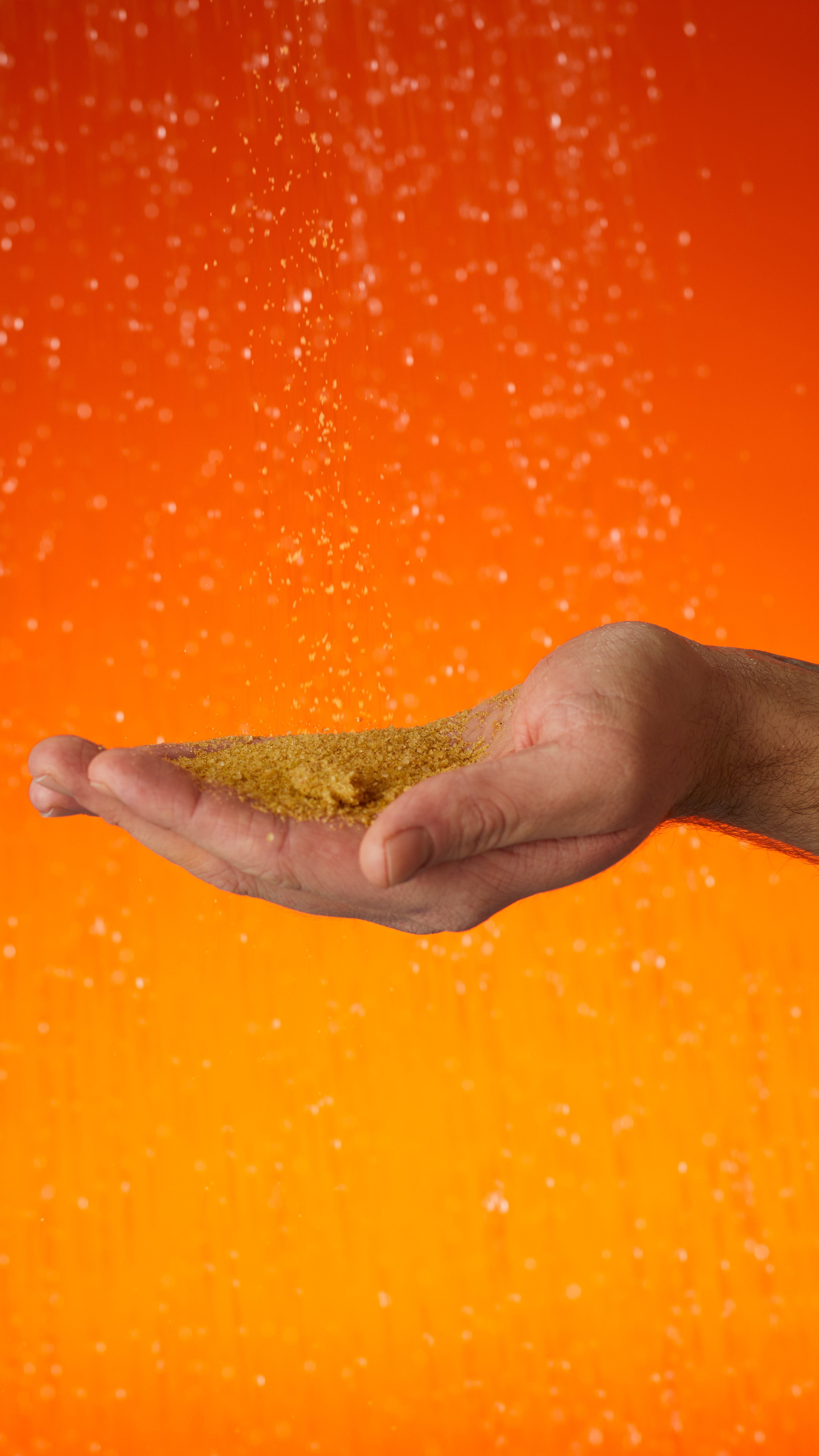 A hand holds the sandy showder as shower drops fall. On a dark to light orange gradient background.