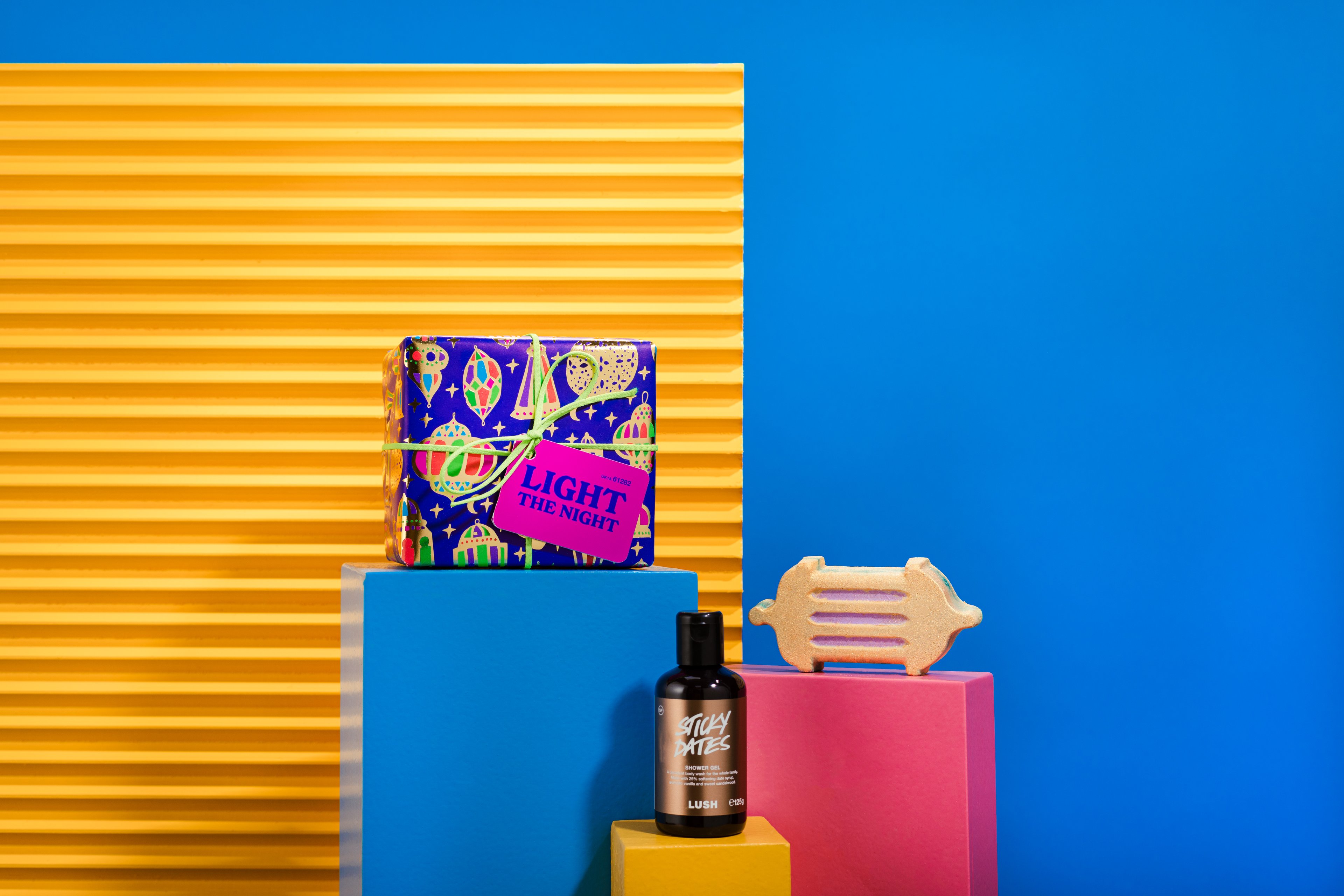 Light The Night gift, in front of a blue and yellow background, surrounded by its products on blue, yellow and pink plinths.