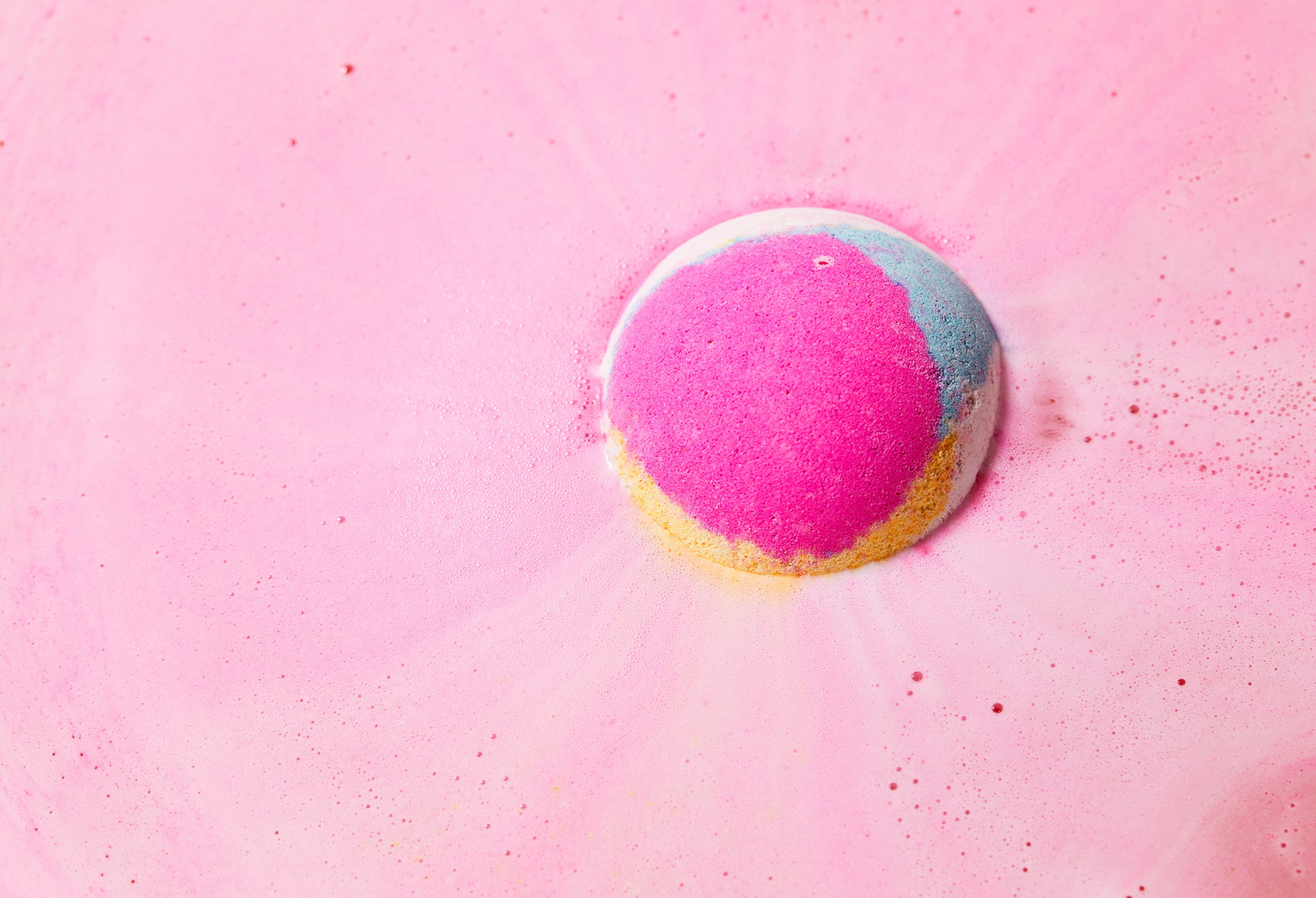 Pink, blue, yellow and white Marshmallow bath bomb floats among velvety, pink bubbles.