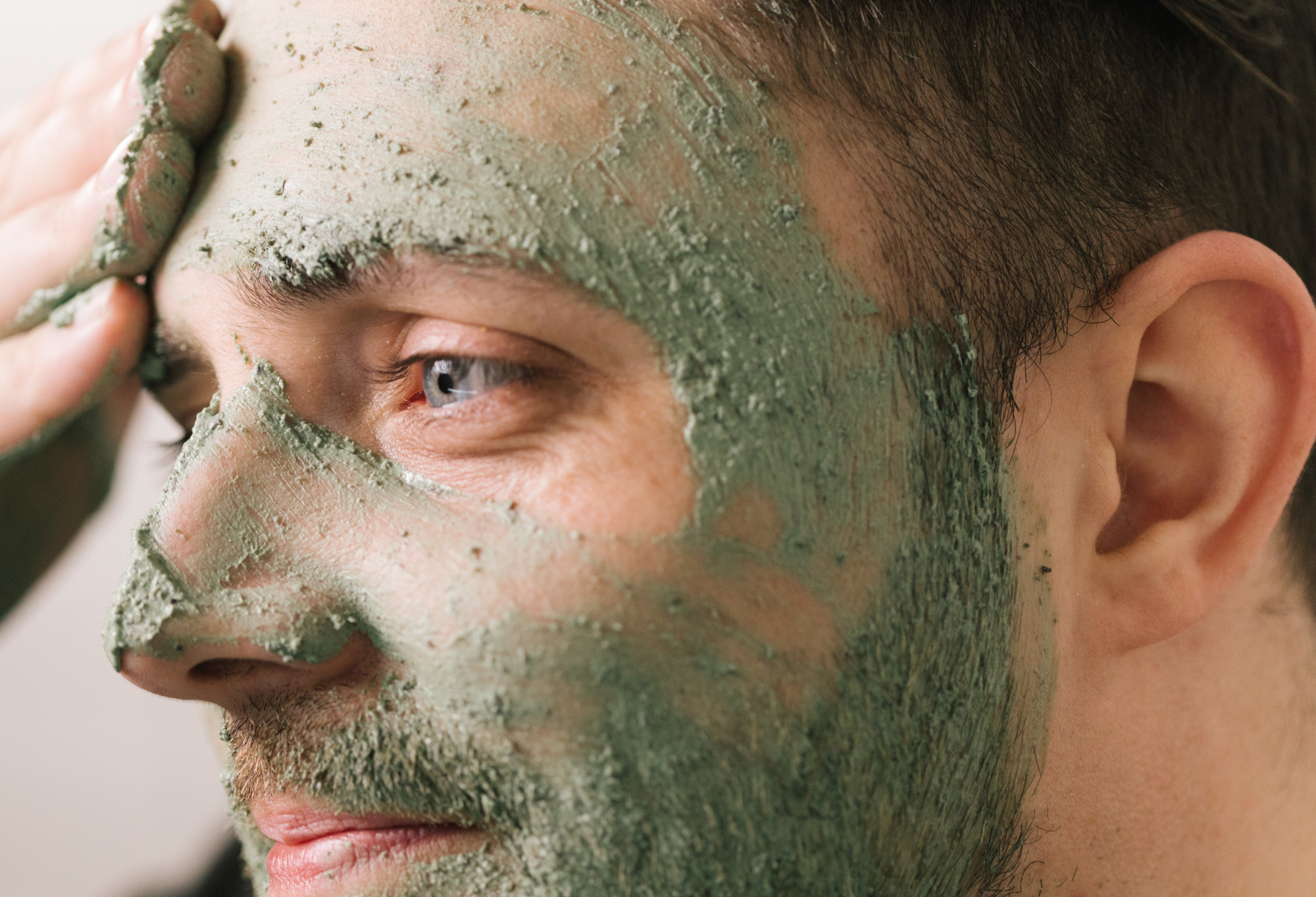 Mask of Magnaminty (a mint green, textured face and body mask) is applied with a hand to the forehead.