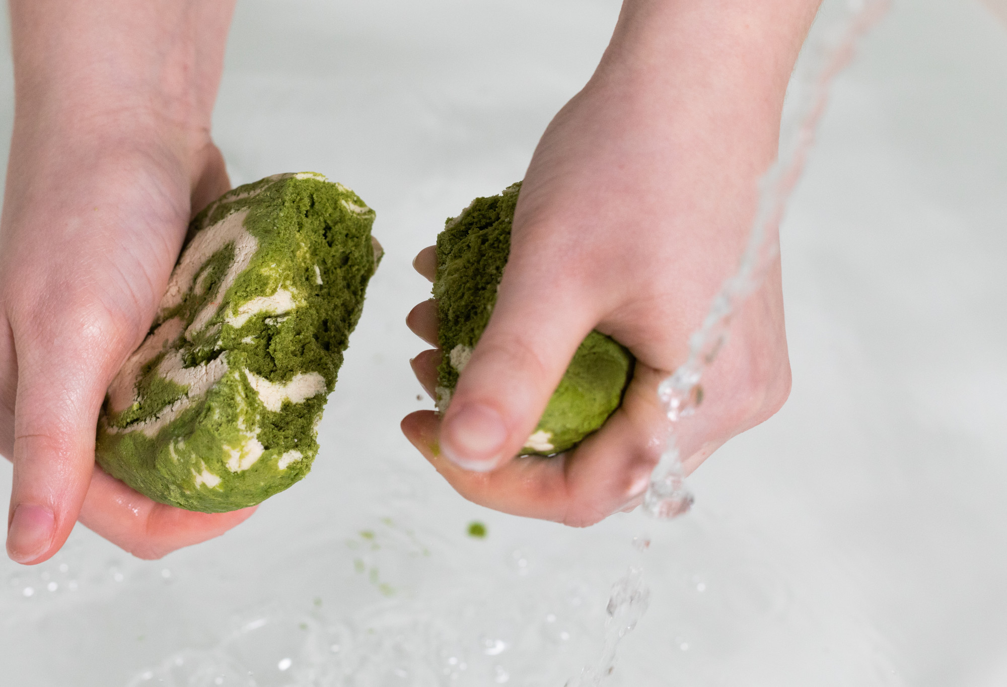 Two hands have snapped Matcha Roll bubble bar in half as water runs near by with water in the background.