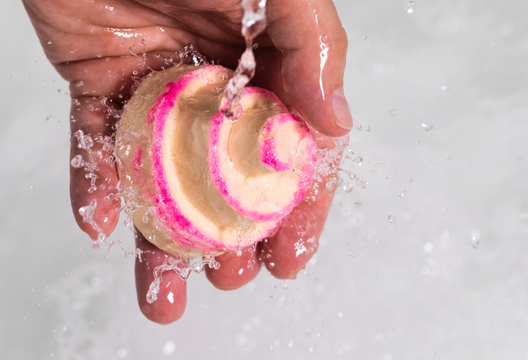 A hand holds the cream and pink swirled Mrs Whippy bubble bar at 90 degrees as water splashes over it.