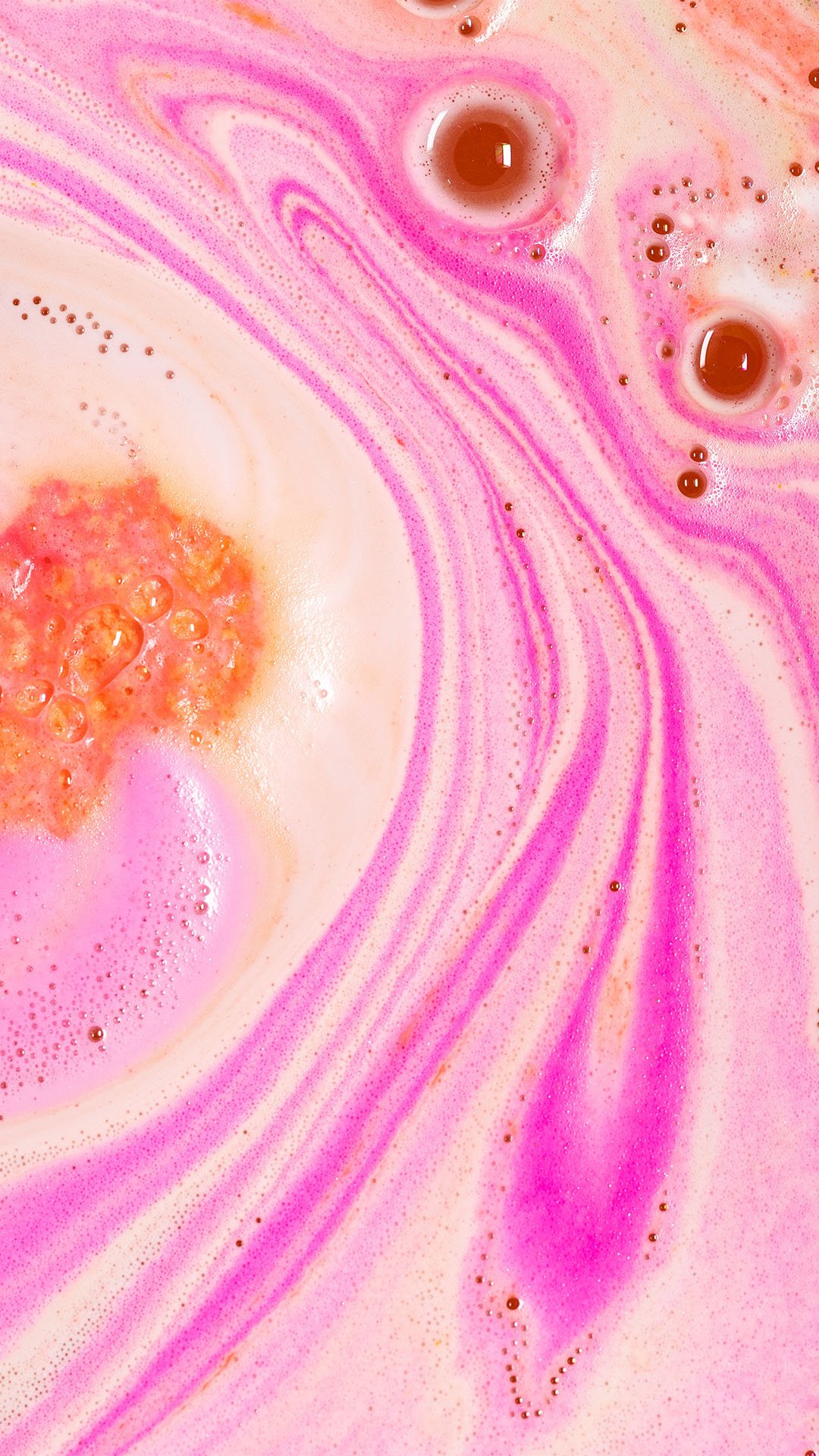 Close up of Peachy bath bomb in the tub. Pink and coral-coloured froth and bubbles.