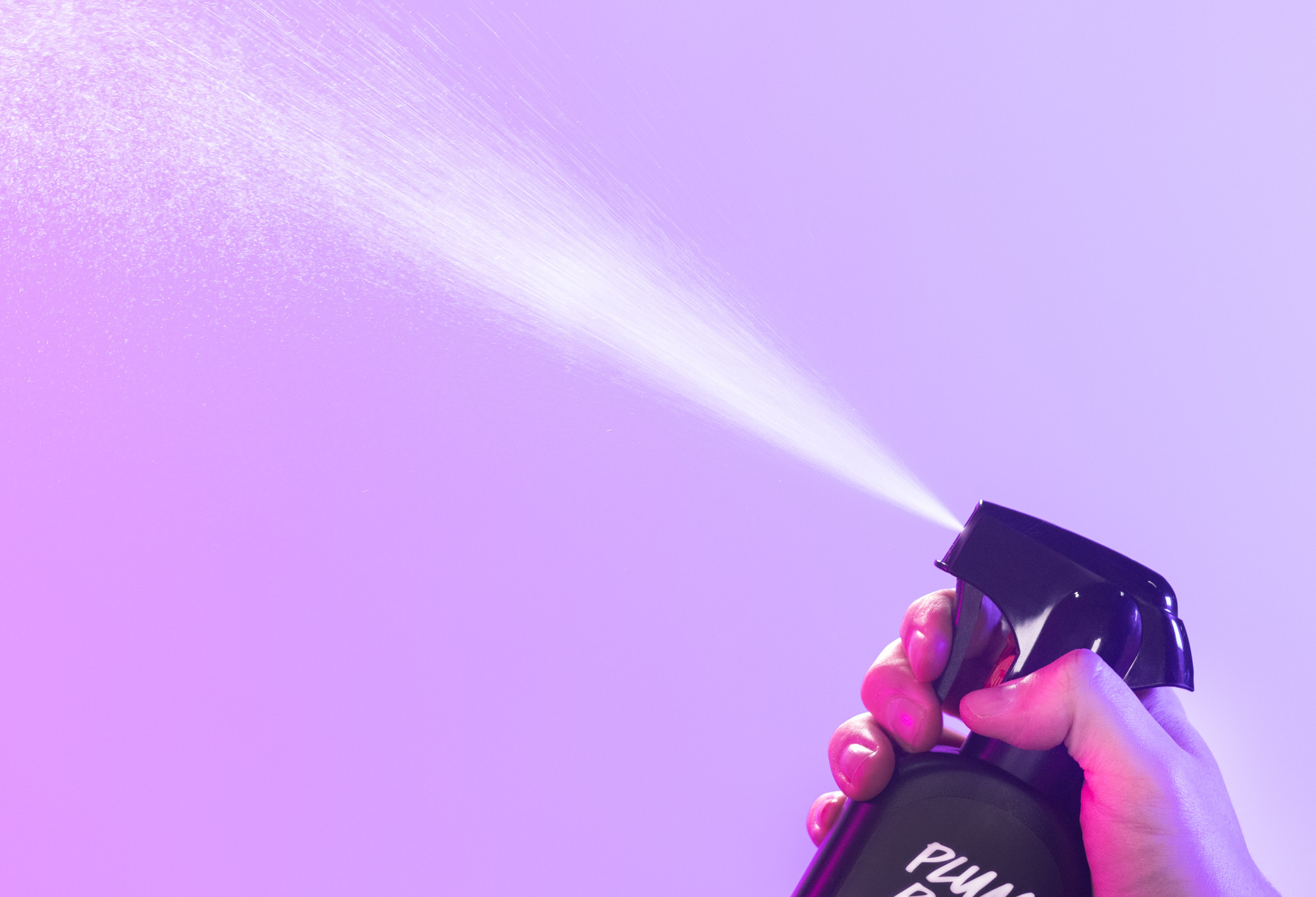 Plum Rain body spray is sprayed up into the air, in front of a bright, light purple background.