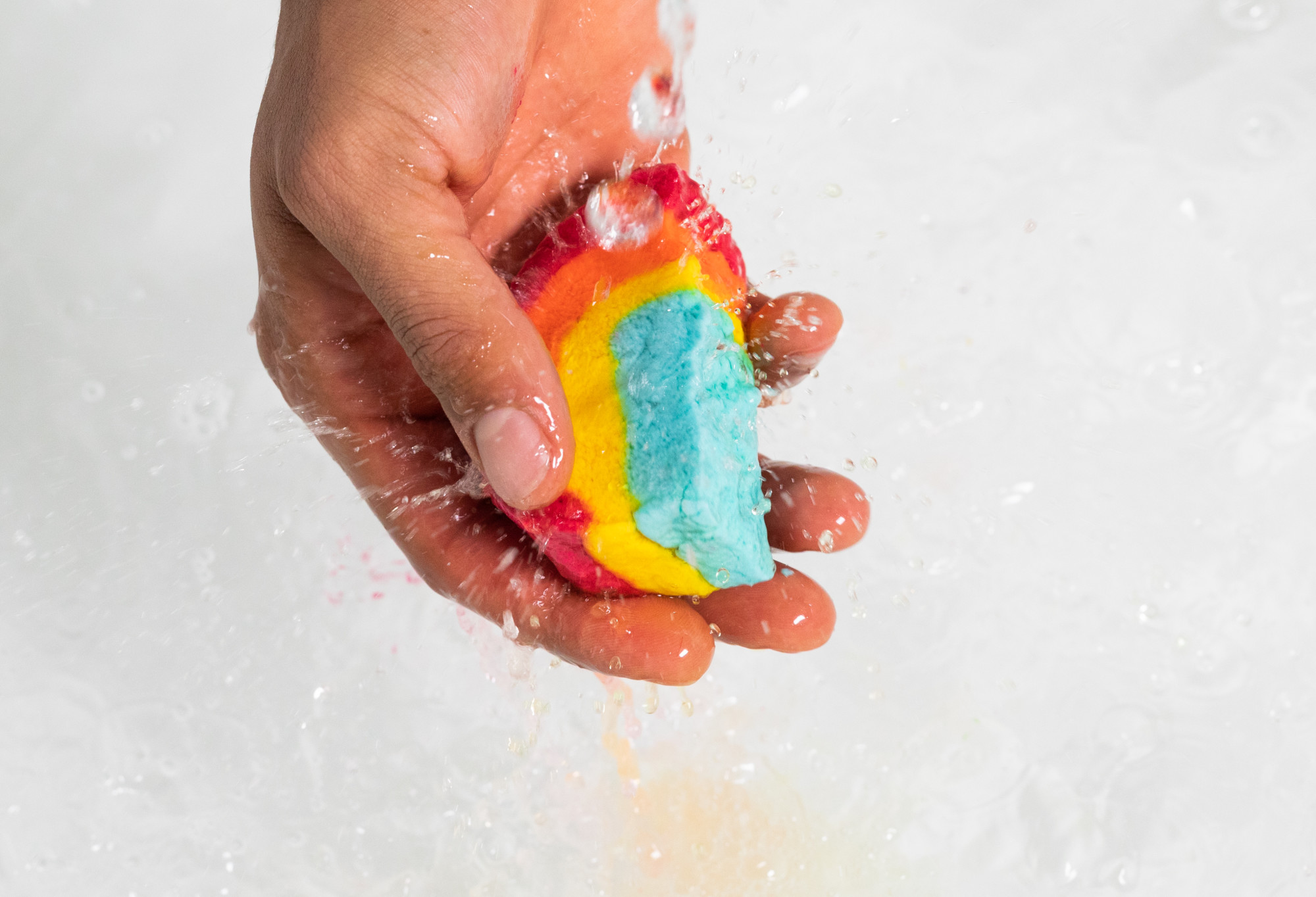 A hand holds a snapped half of Rainbow under running water as bubbles form in the background and a yellow tint appears.