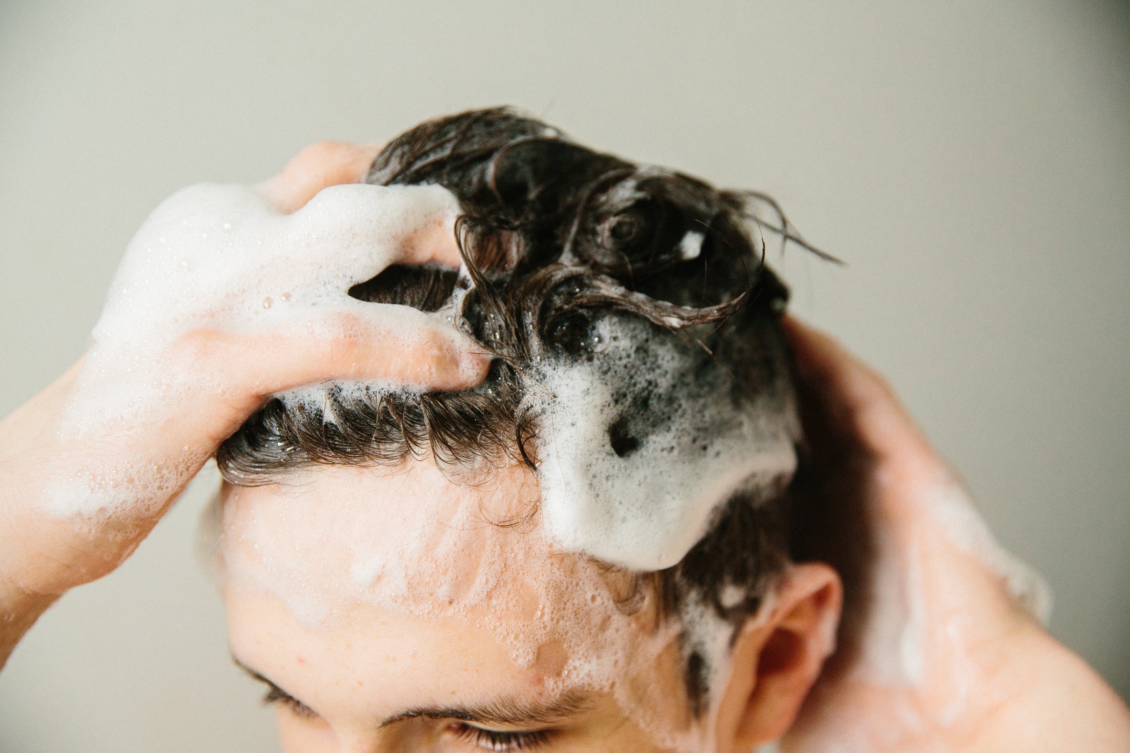 The image shows the top of the model's head as they lather in the creamy shampoo into short brown hair with bubbles and suds.