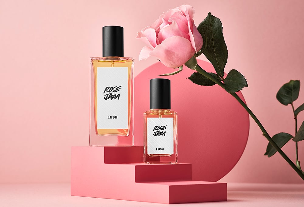 Rose Jam perfume is placed on pink podium that is staggered to create steps. Behind the podium is a pink rose and circle.