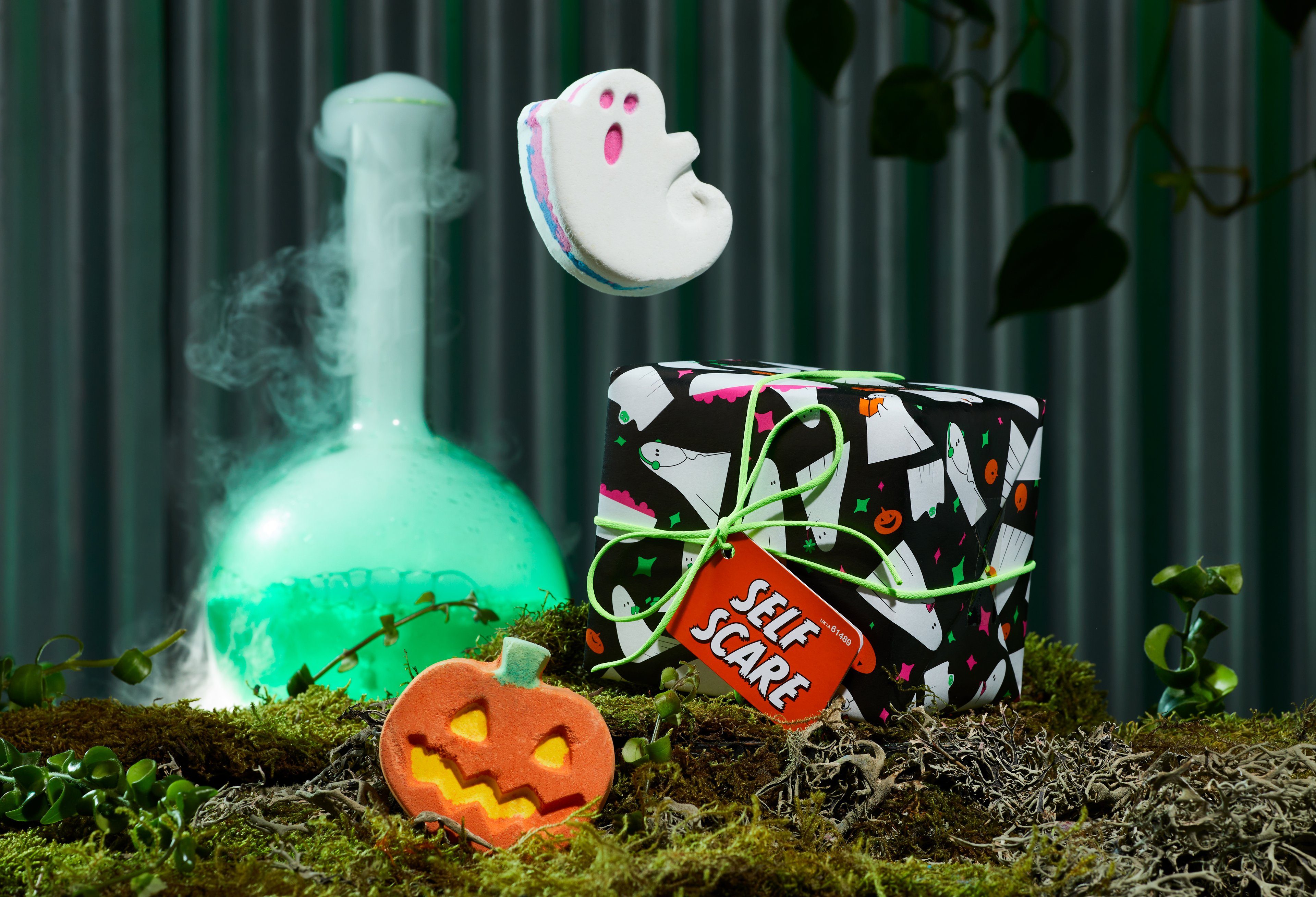 Self Scare gift, in front of a dark green background, surrounded by its products on a bed of moss. 