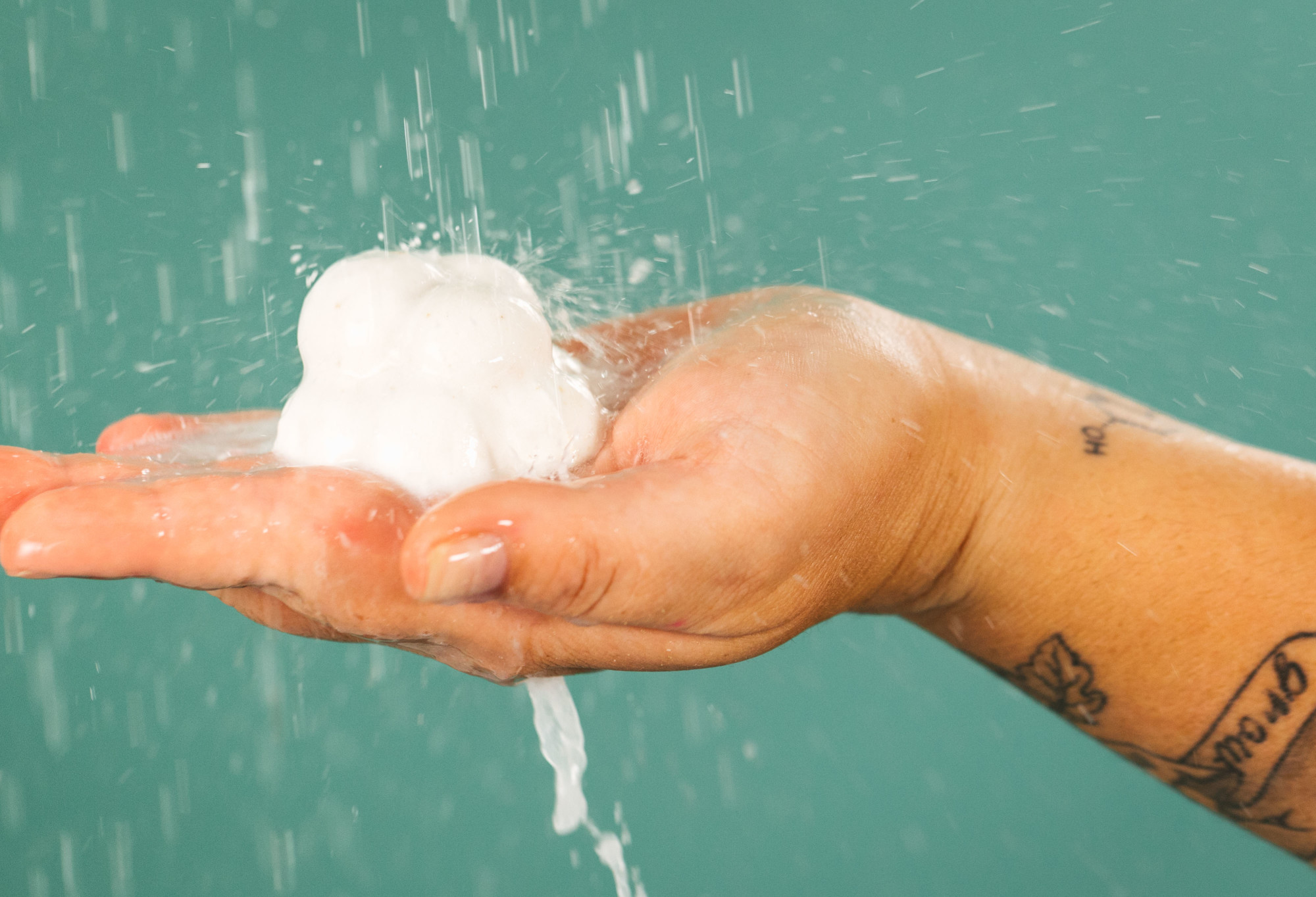 Sleepy, a white, bobbly, cloud shaped shower bomb, is held in the palm of the hand, under water pouring down like rain.