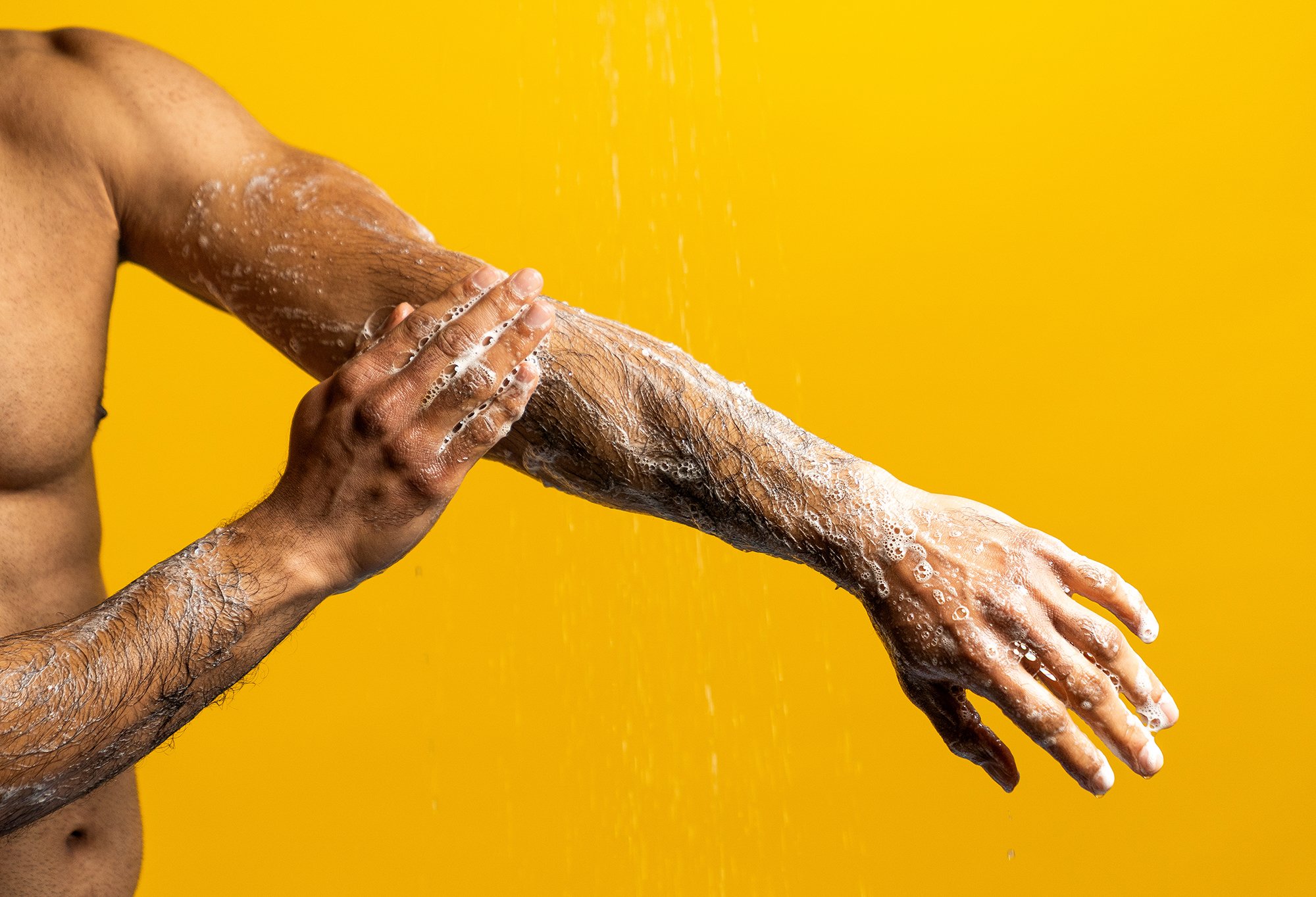Sticky Dates Shower Gel being lathered onto a models arm in front of a yellow background.
