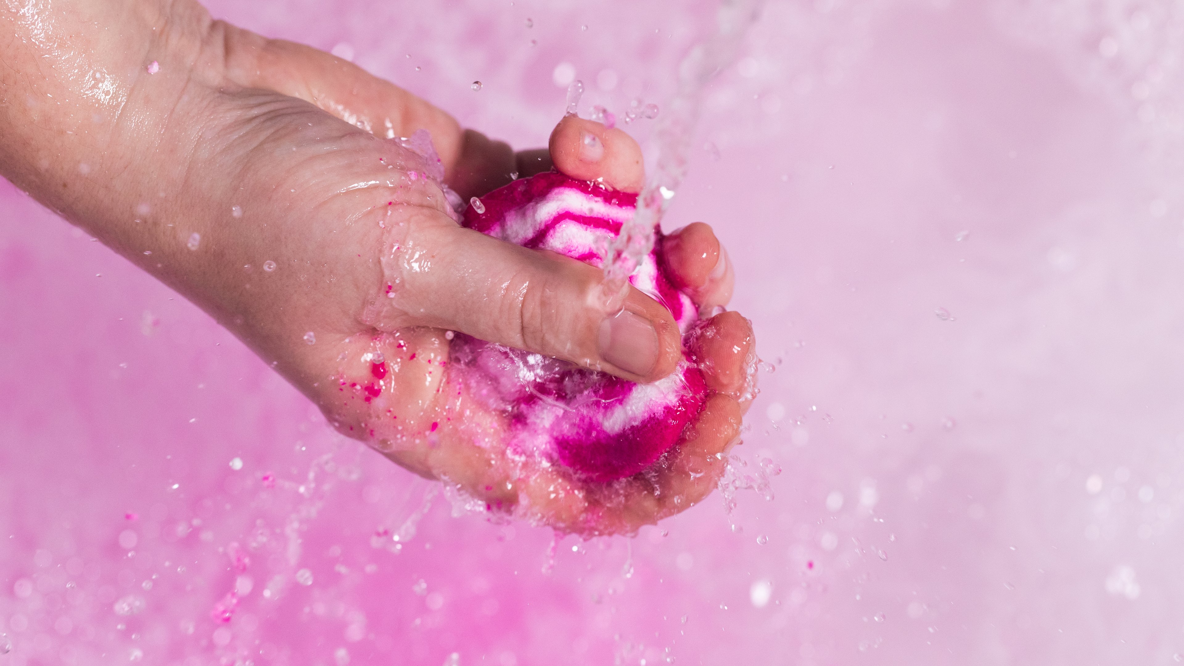 Model holds the Comforter bubble bar under running bath water as beautiful pink bubbles form below.
