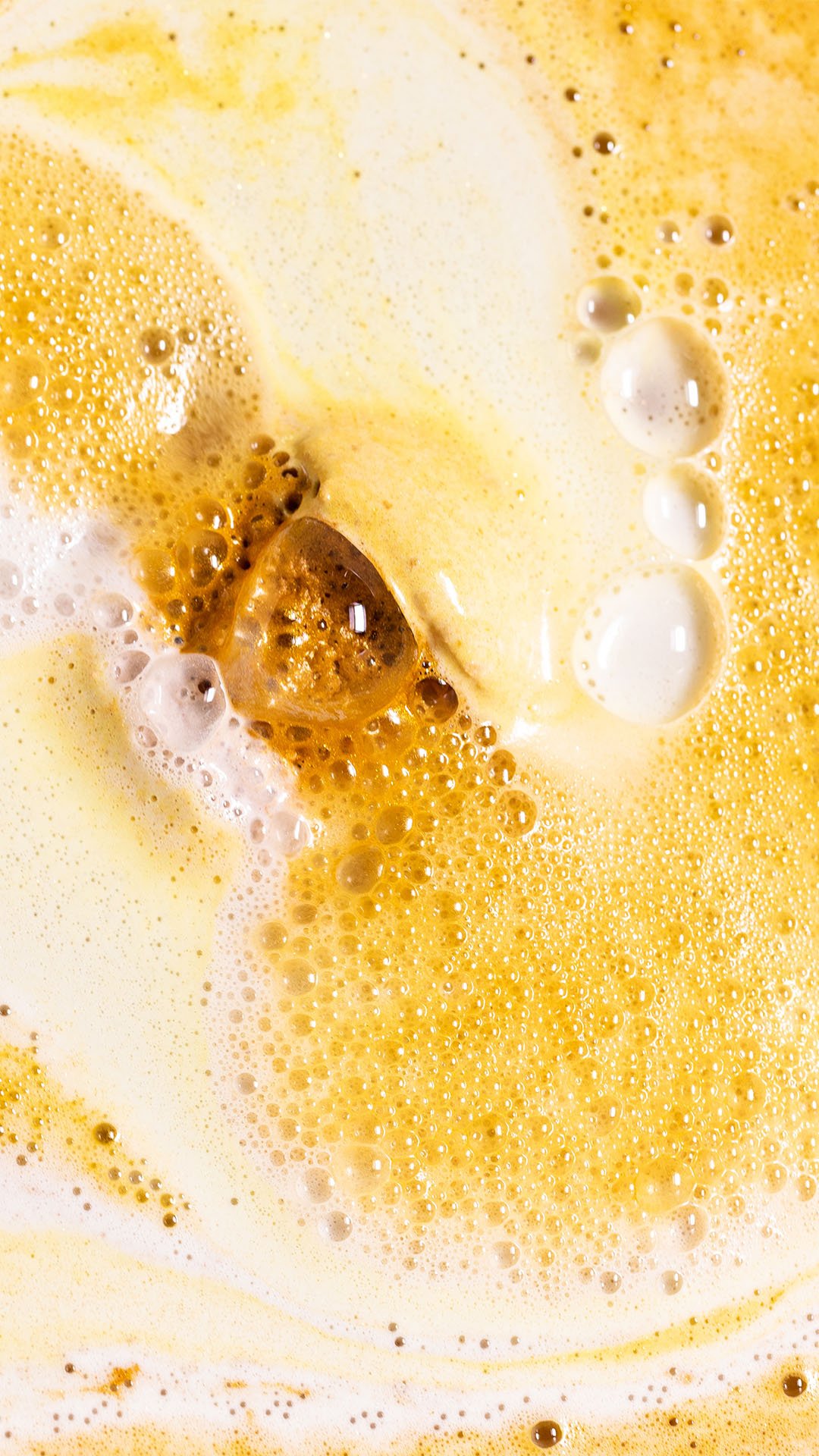 Turmeric Latte bath bomb in the bath, creating thick and creamy golden and white bubbly froth.