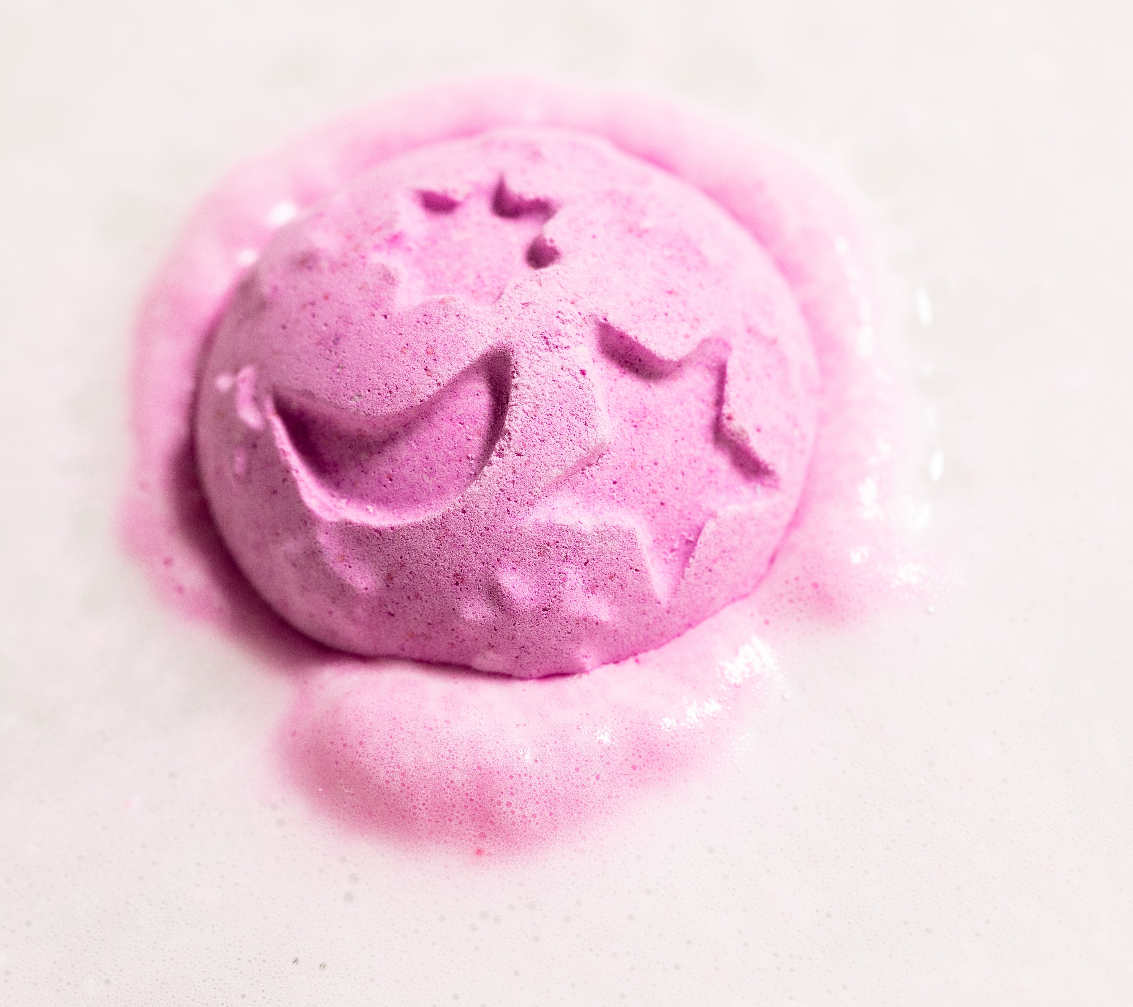 Deep pink Twilight bath bomb sitting in the water surrounded by soft, foamy, pastel pink bubbles.