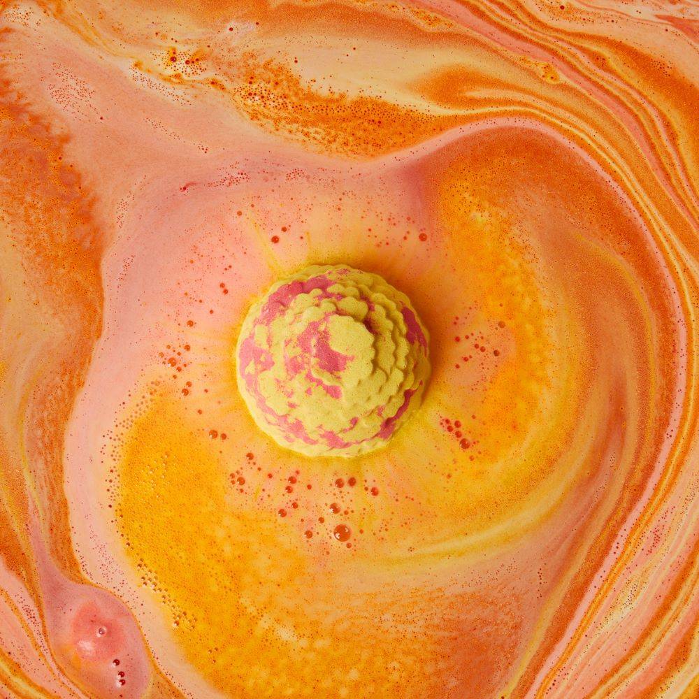 An above shot of the vibrant Cempasúchil bath bomb surrounded by colourful swirls of yellow and orange.