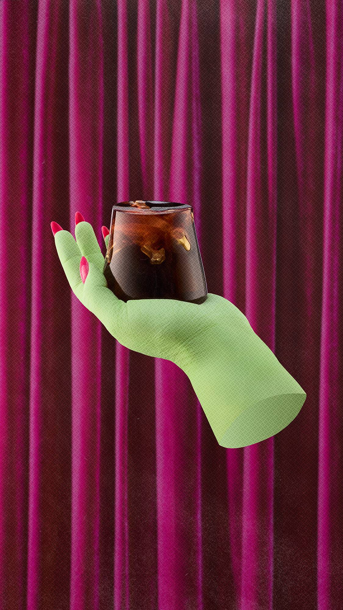 A pale green witch's hand with long, bright pink fingernails balances a dark, translucent trapezoidal "Creature Of The Night" shower jelly containing a golden lizard gummy. The scene is set against a background of pleated, deep pink velvet curtains.