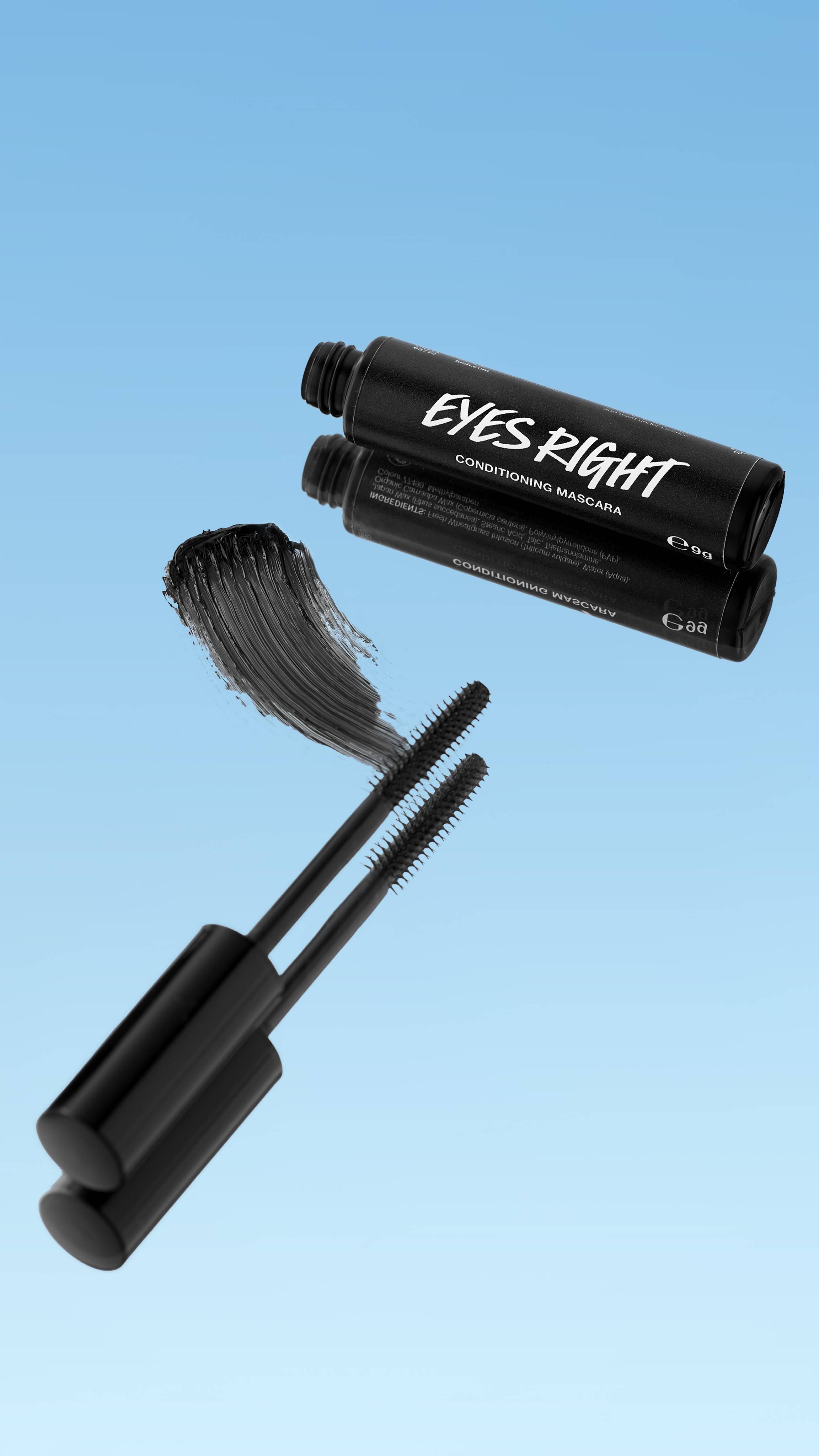 The black tube of Eyes Right ~ Mascara is shown lying down with its reflection visible. Two black mascara wands are extended below, next to a thick smear of black mascara. The products float against a bright blue background.