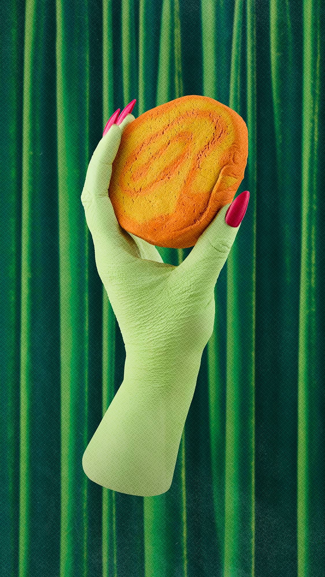 A green hand with long pink nails holds an orange and yellow "Swirly Pumpkin" bubble bar, set against a dark green draped velvet curtain background.