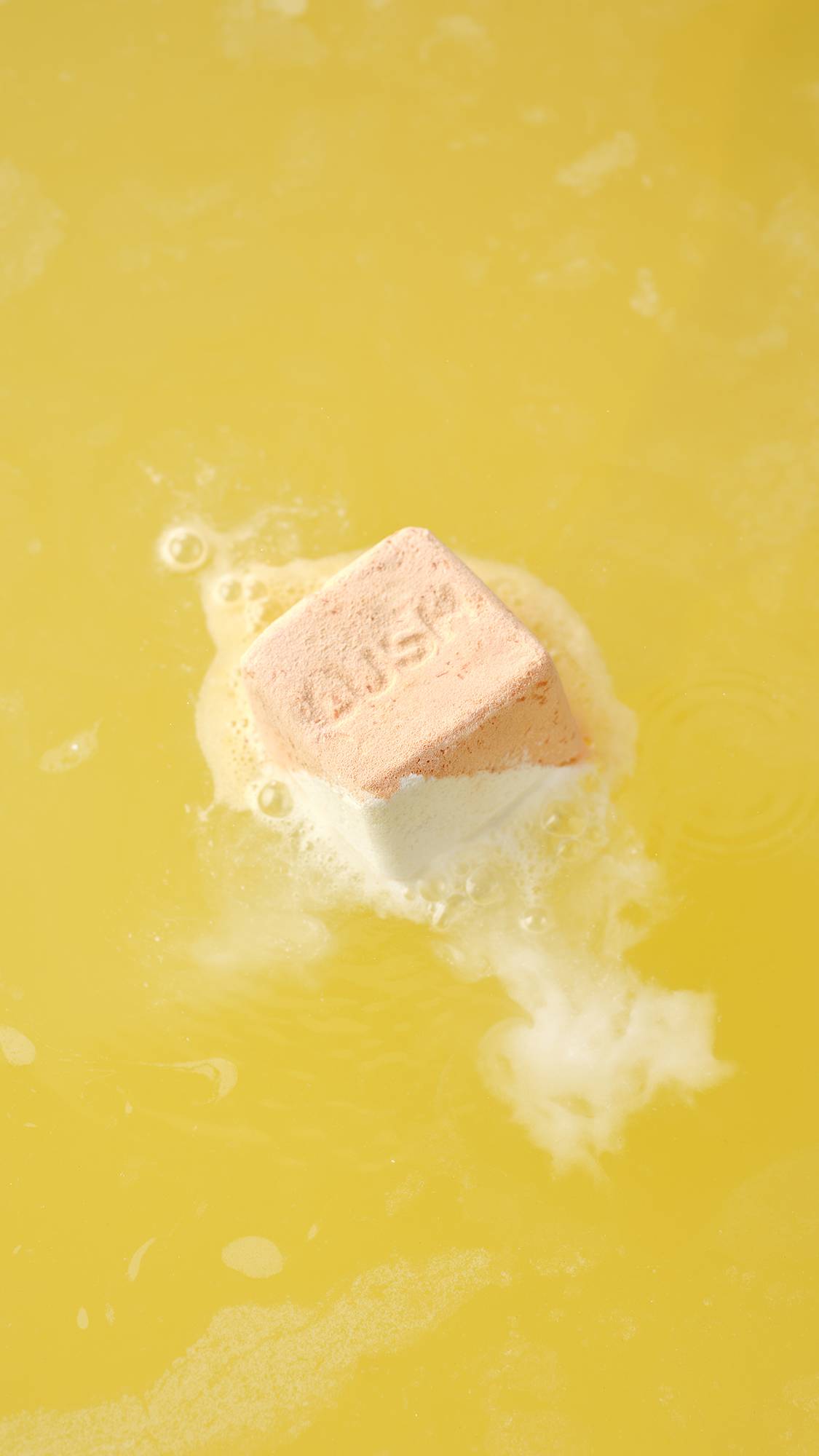 The Cold Water Soother bath bomb dissolves on the surface, releasing white, frothy foam and vibrant swirls that ripple across the water.