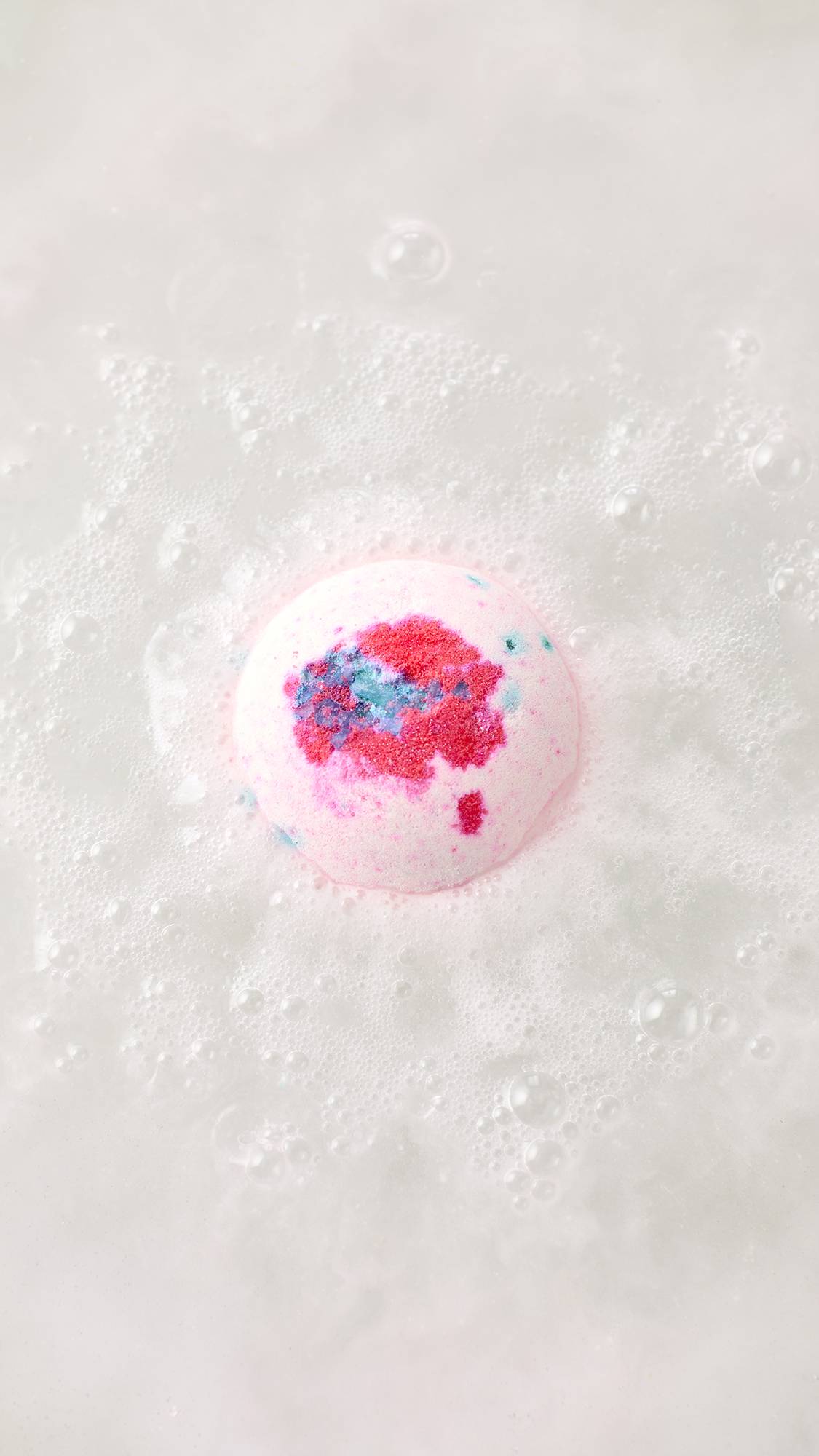 An aerial view of the dissolving Equity bath bomb. Thick, velvety swirls of pastel pink, bright blue, and crisp white foam ripple across the surface of the vibrant blue bathwater.