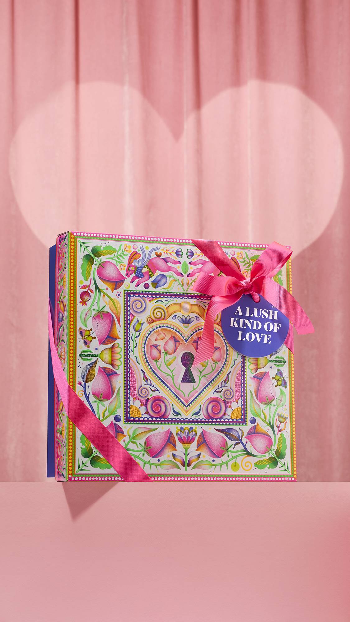 The A Lush Kind of Love gift set displays a colourful box beside Passion shower gel, Posh Chocolate lotion, a strawberry bubbleroon, a white heart bomb, a love letter bomb, and a shimmering ladybug bar.