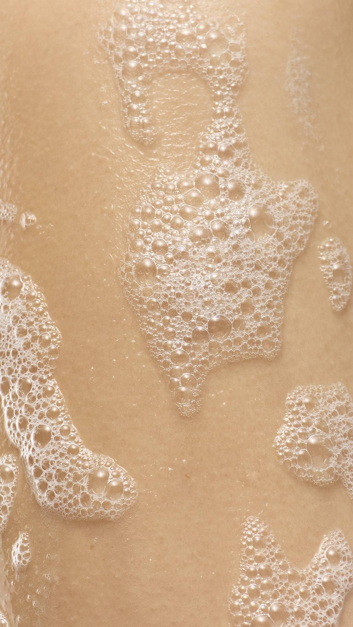 A close-up of white, soapy lather and clusters of bubbles from the Bouncing Spider shower gummy on a person's skin.
