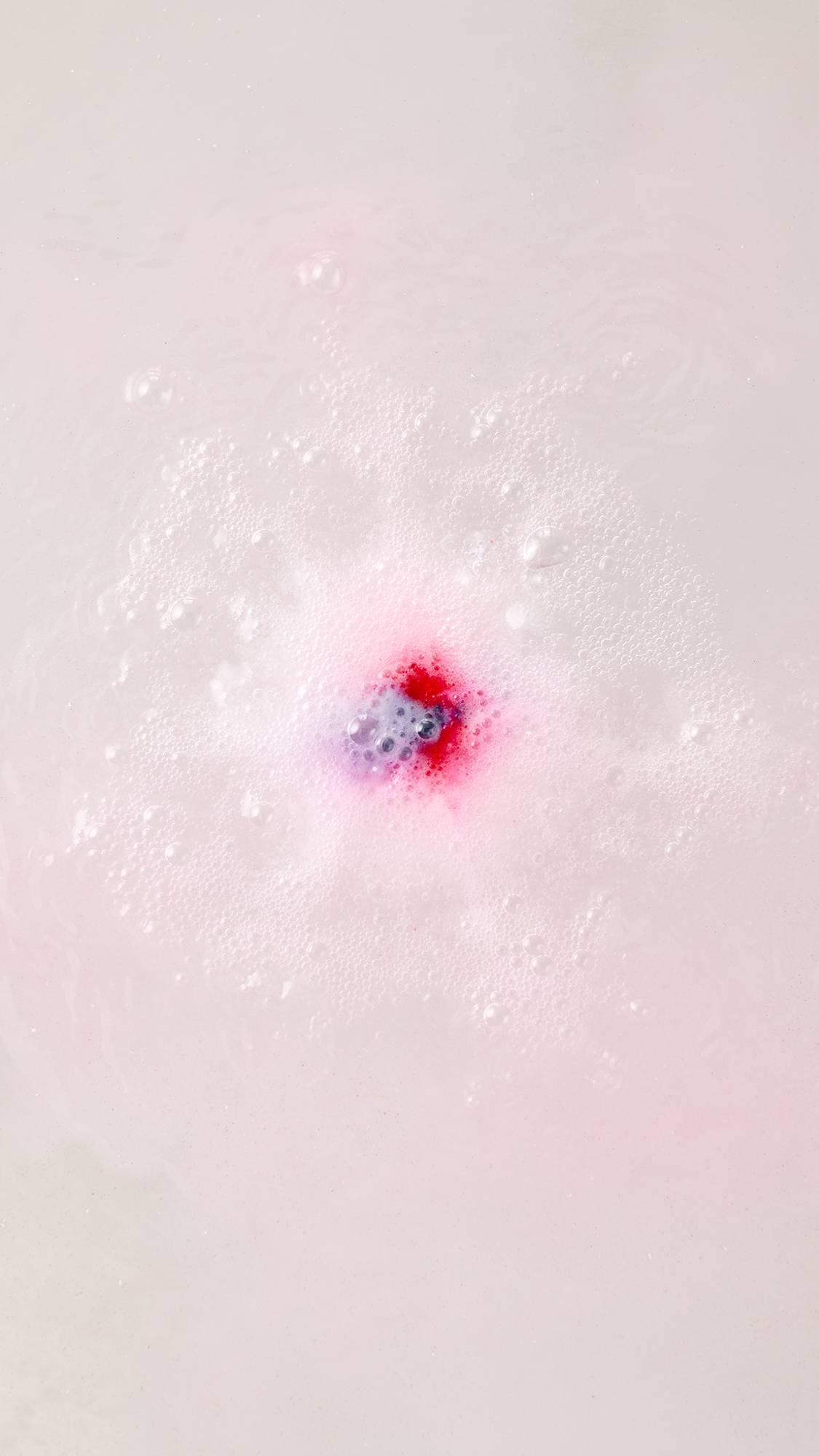 An aerial view of the dissolving Equity bath bomb. Thick, velvety swirls of pastel pink, bright blue, and crisp white foam ripple across the surface of the vibrant blue bathwater.