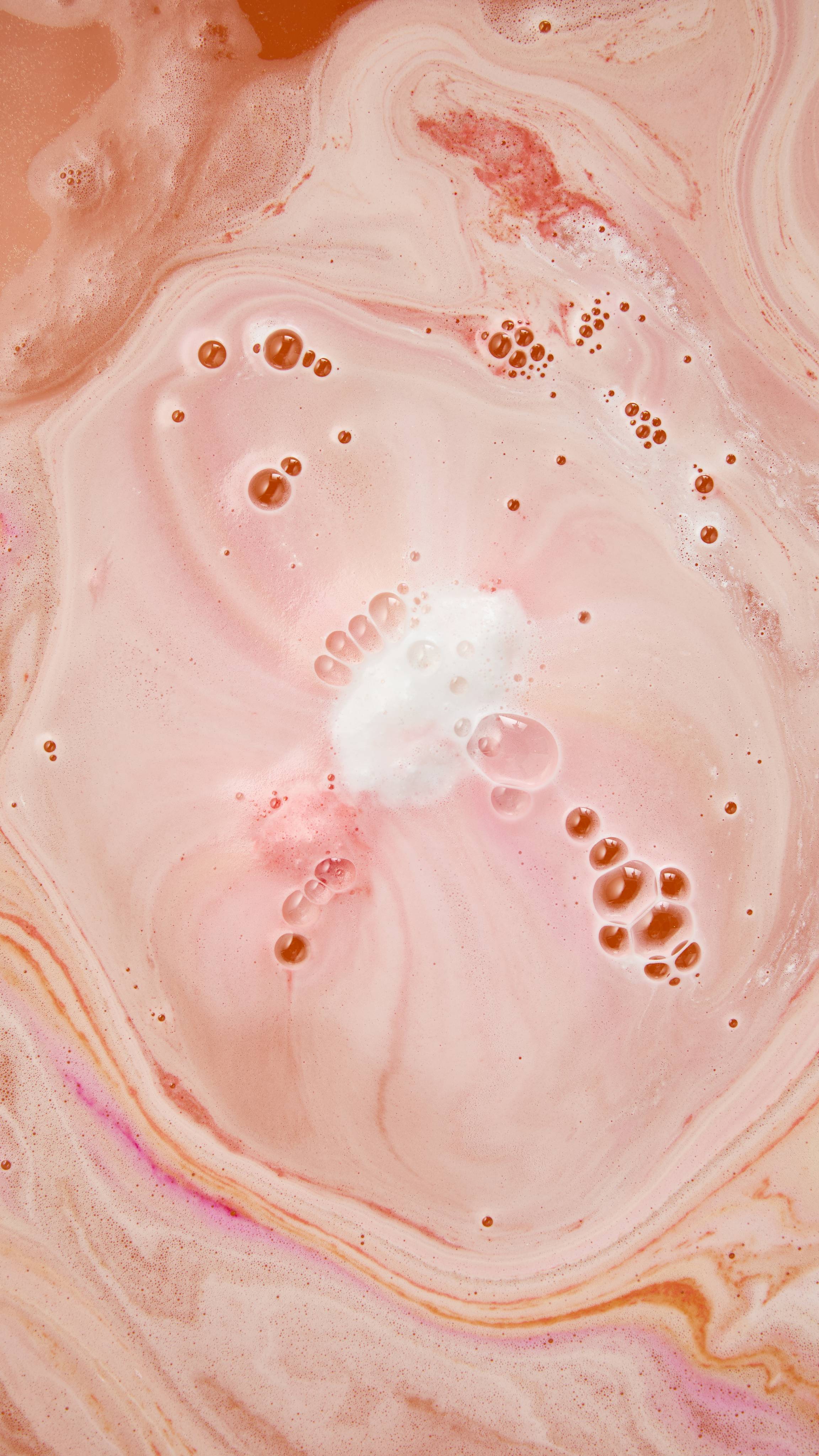 Swirling patterns of pastel pink and peach bath foam with streaks of vibrant magenta, featuring delicate white froth and glossy bubbles at the centre.