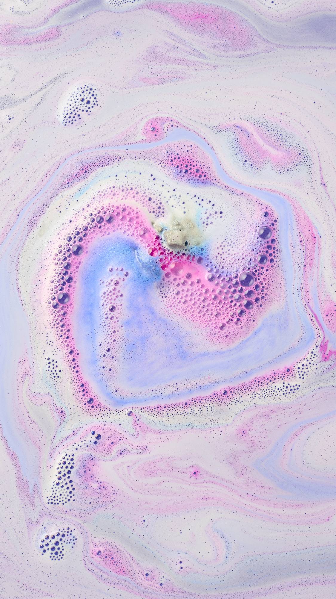 Vibrant streams of periwinkle blue, magenta pink, and white foam swirl into a spiral as the Lush "Silent Night" bath bomb dissolves across pastel purple bathwater.