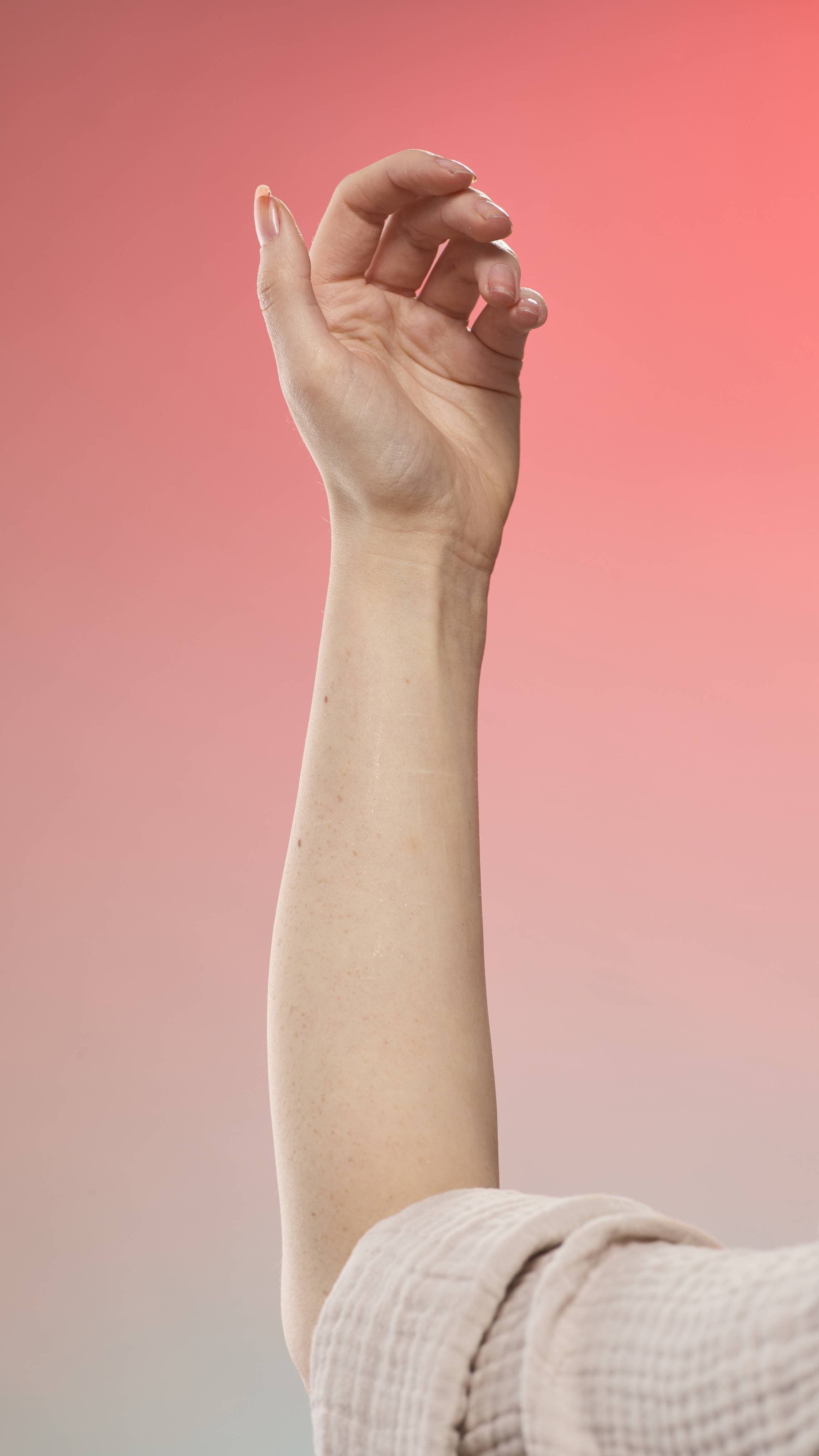 An arm with a subtle shimmer against a peach-to-blue gradient background. The person is wearing a light, textured robe.
