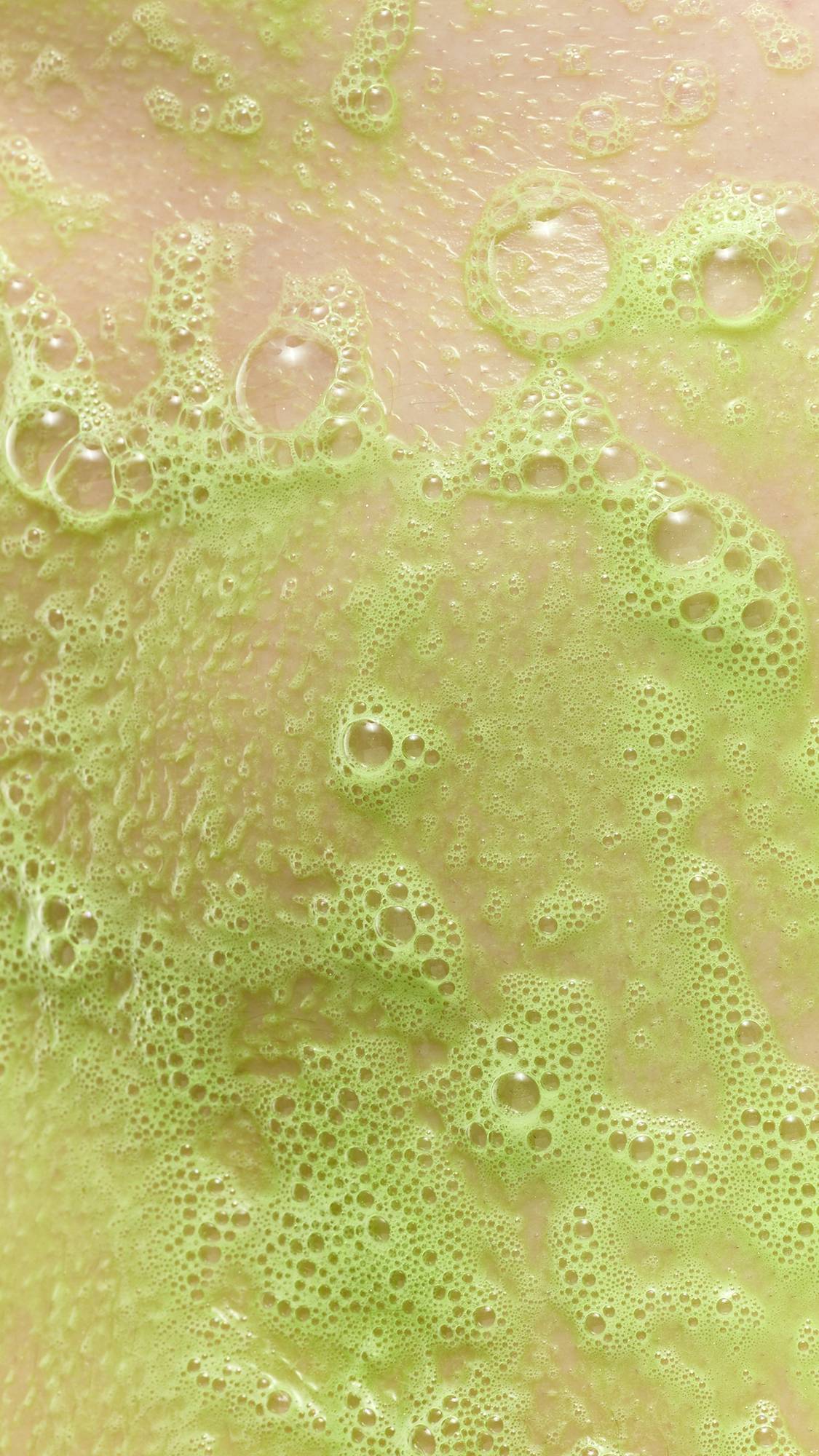 A close-up of vibrant lime green soapy lather and bubbles from Tree Hugger soap on a person's skin.