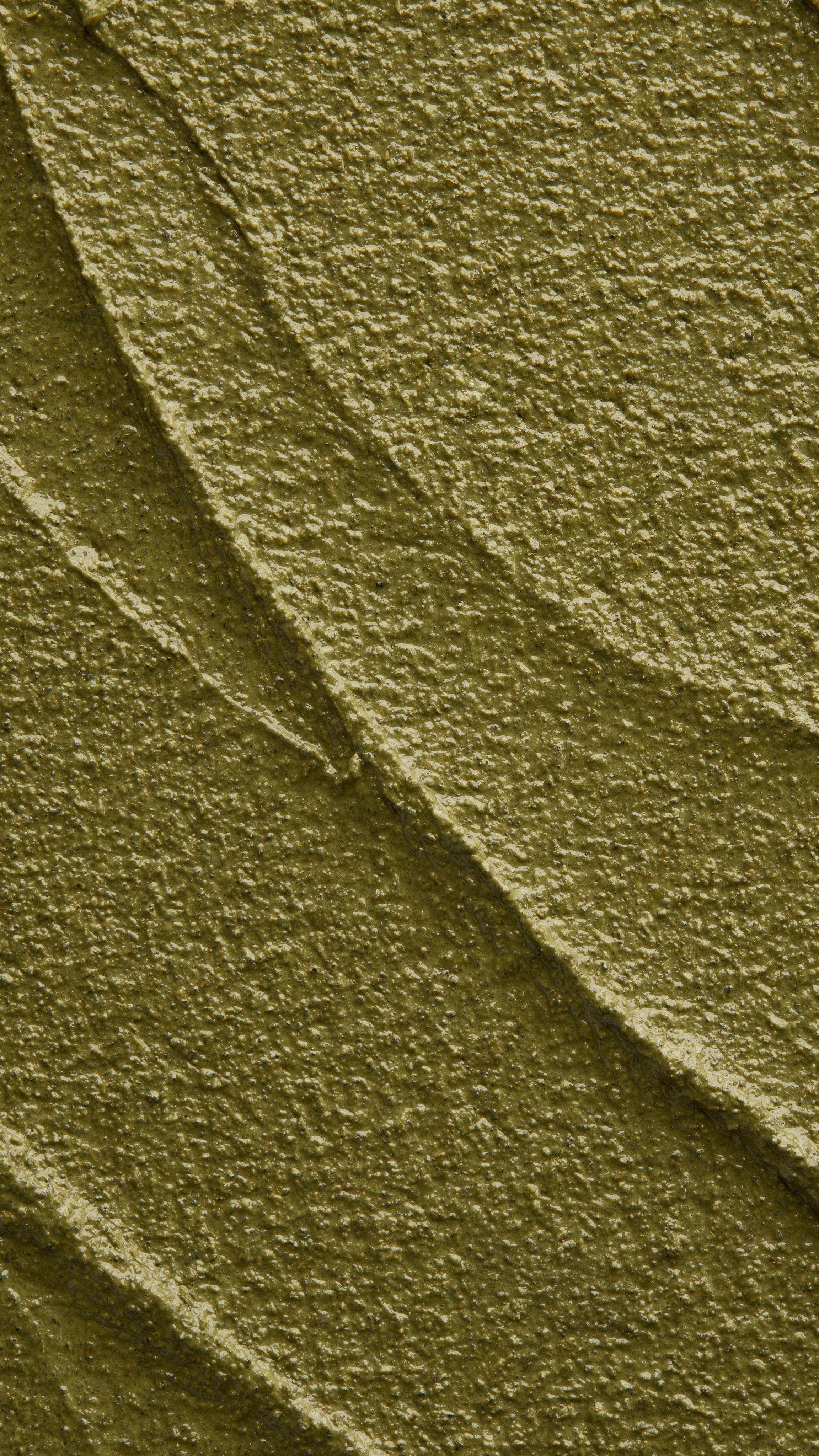 A close-up, textured shot of a thick, olive-green "Babylon" scalp treatment spread in diagonal ridges. The product has a dense, grainy, and slightly moist consistency with visible dark herbal granules.