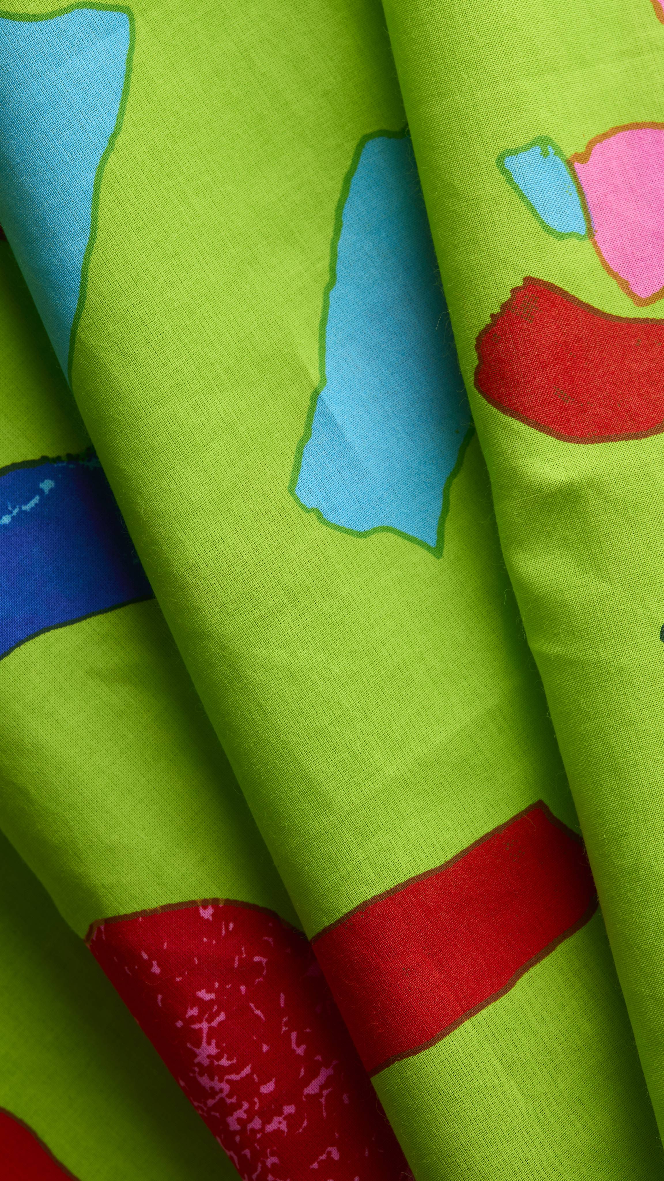 A close-up reveals the texture of the Love Knot Knot Wrap, displaying a vibrant pattern of blue, pink, and red abstract shapes against a bright green fabric background.