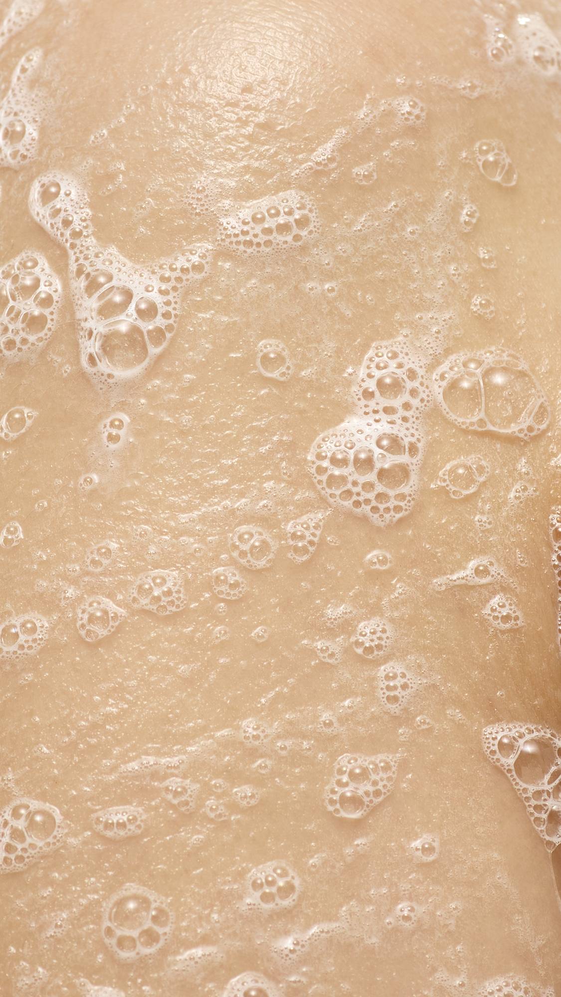 A close-up of white, soapy lather and bubbles from Smell Of Roses soap on a person's skin.