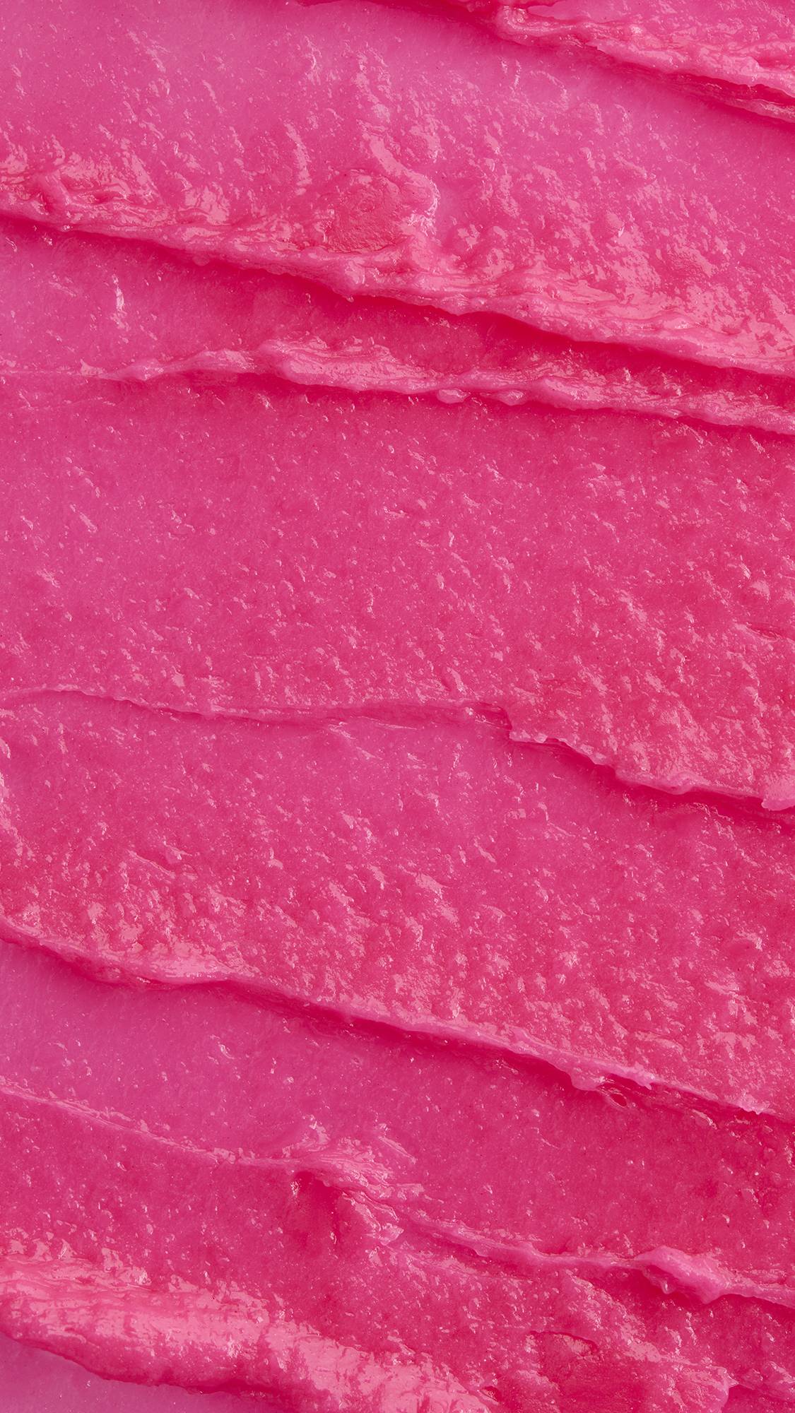 A macro close-up texture shot of rich, vibrant pink lip butter spread in smooth, creamy horizontal ridges across the frame.