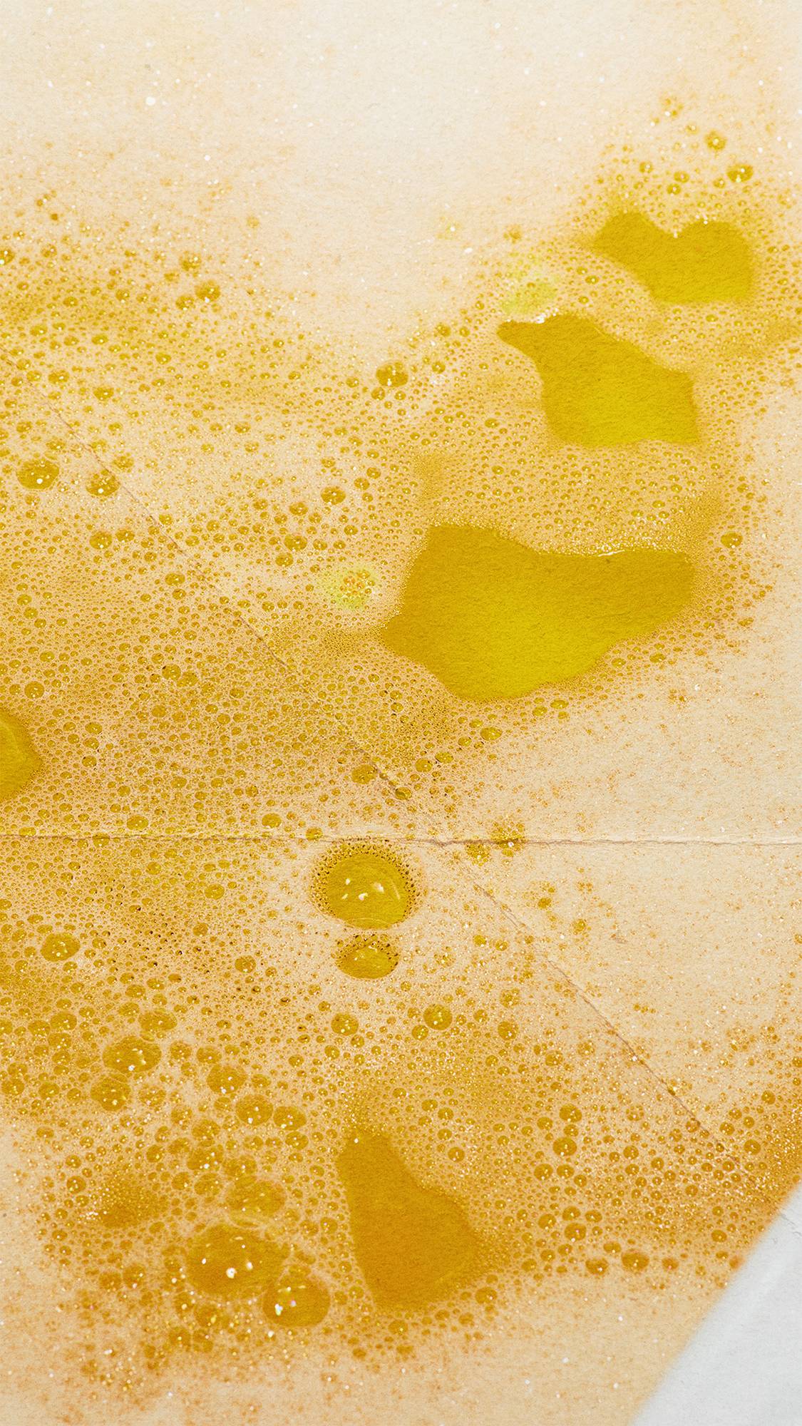 Close-up of vibrant orange bathwater covered in a blanket of fine, white bubble bar foam with clear patches revealing the warm, glowing yellow water beneath.