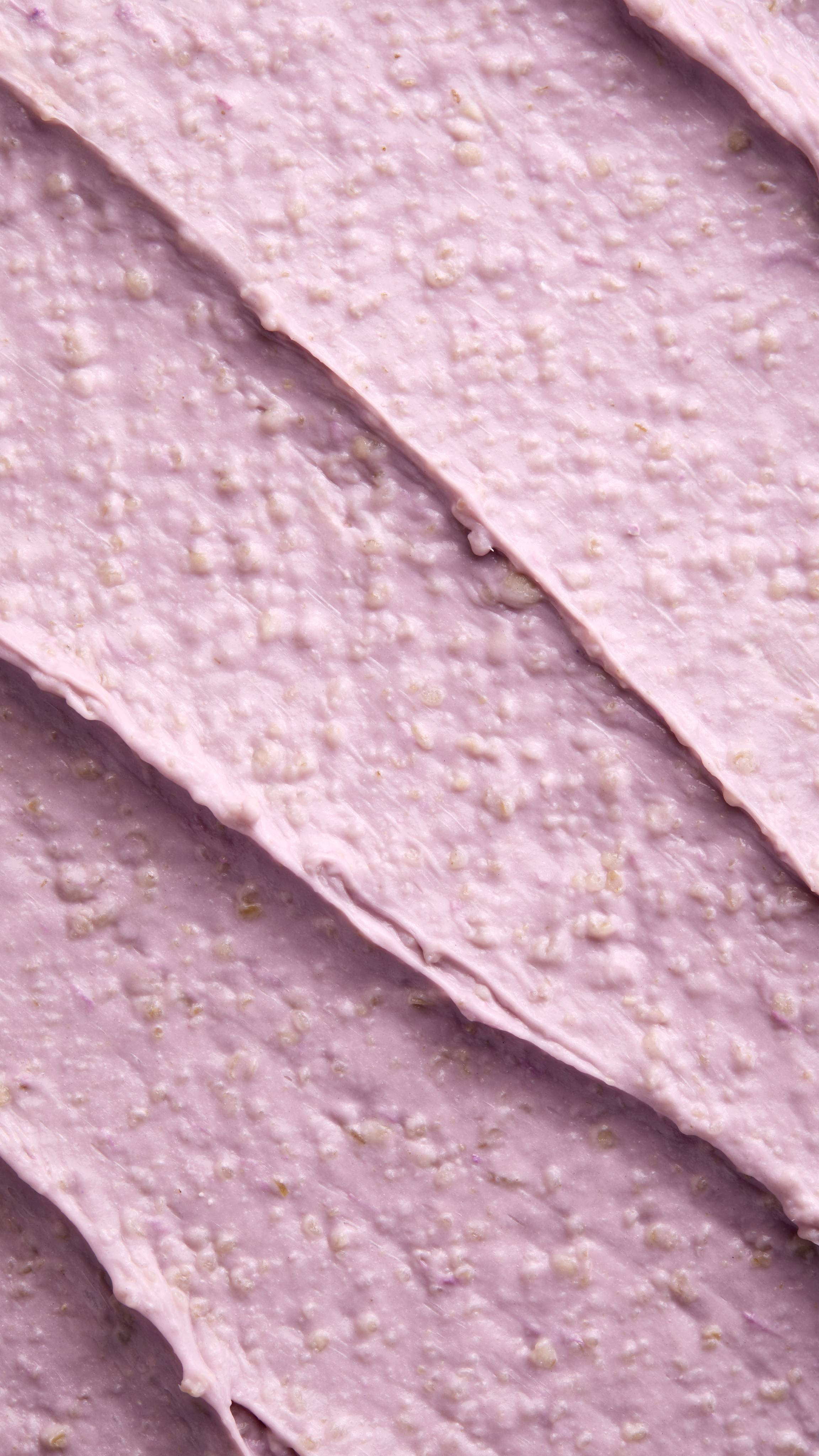 A close-up, textured shot of a thick, lilac-coloured "Calm Down" scalp treatment spread in diagonal ridges. The product has a grainy, lumpy consistency with visible beige exfoliating particles