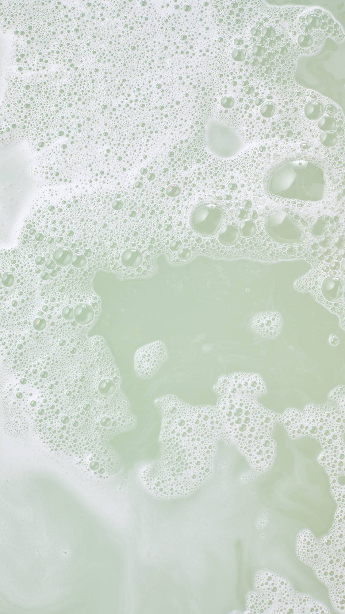 A thick layer of soft white bath foam parts to reveal pale bathwater beneath, surrounded by clusters of fine frothy bubbles.