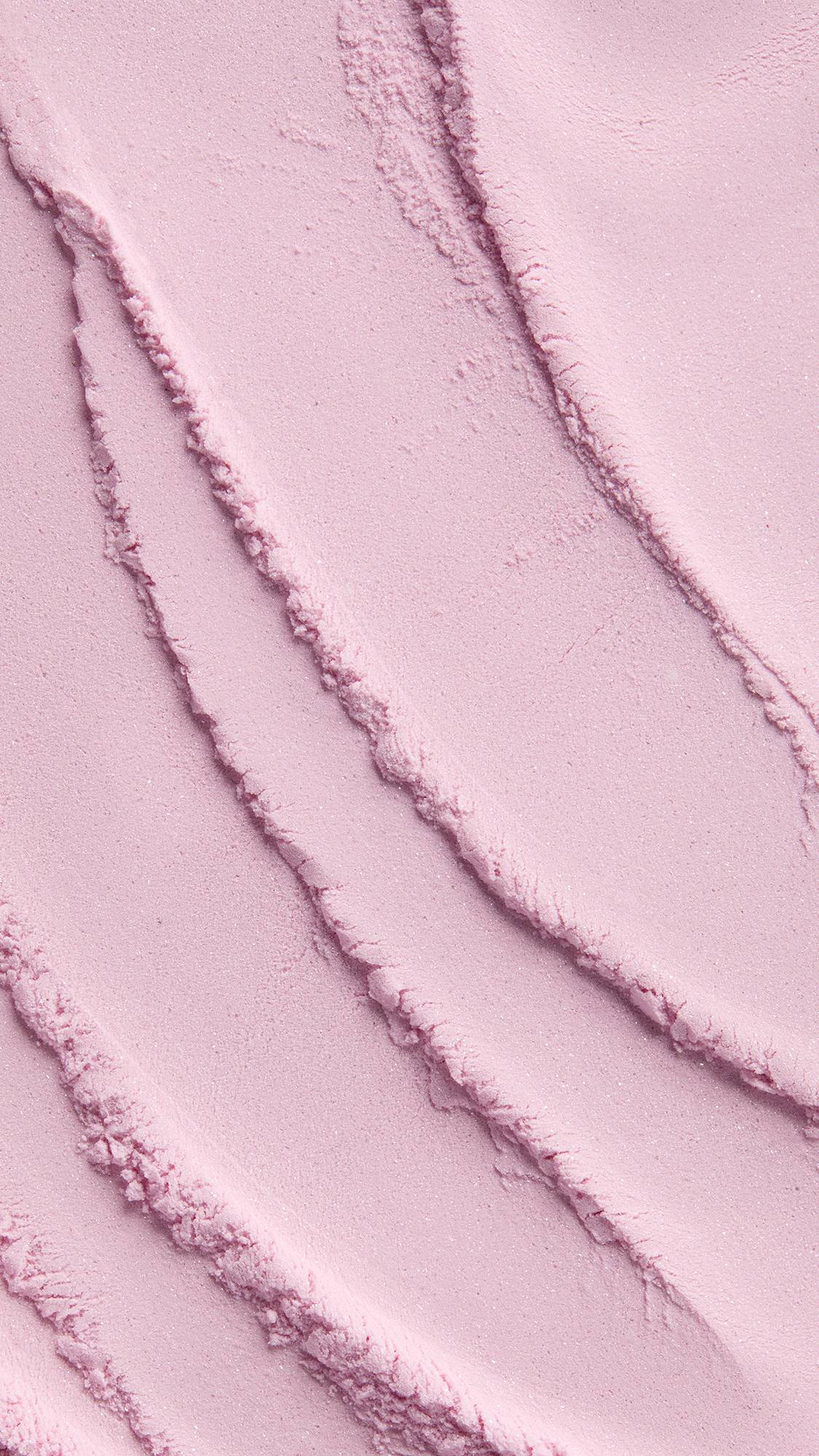 A close-up macro texture shot of finely milled, light pink "Fairy Dust" dusting powder showing smooth waves and subtle ridges across the surface.
