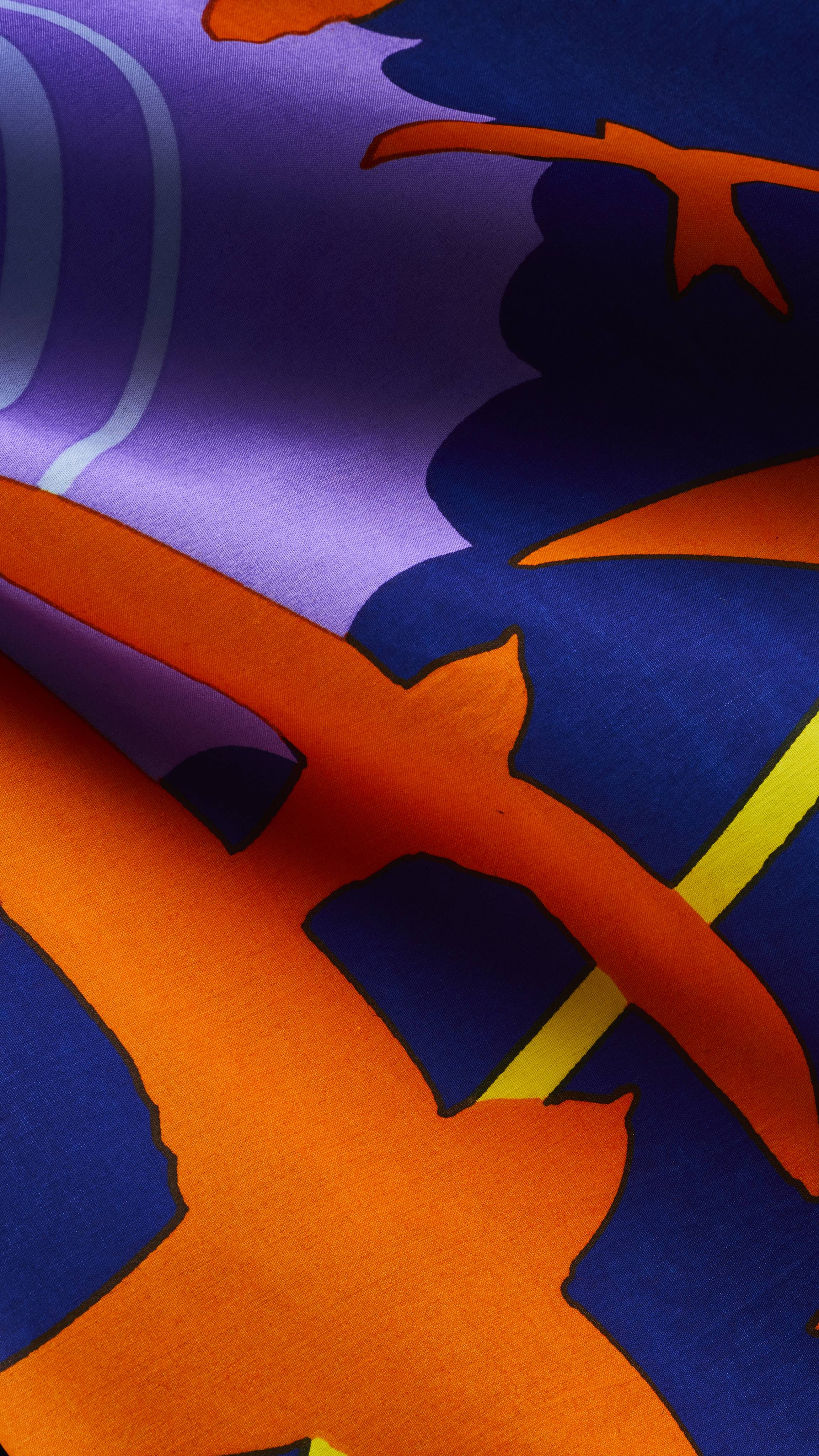 A close-up of a folded smooth fabric knot wrap featuring a bold graphic print of orange bird silhouettes flying across a vibrant royal blue, purple, and yellow background.