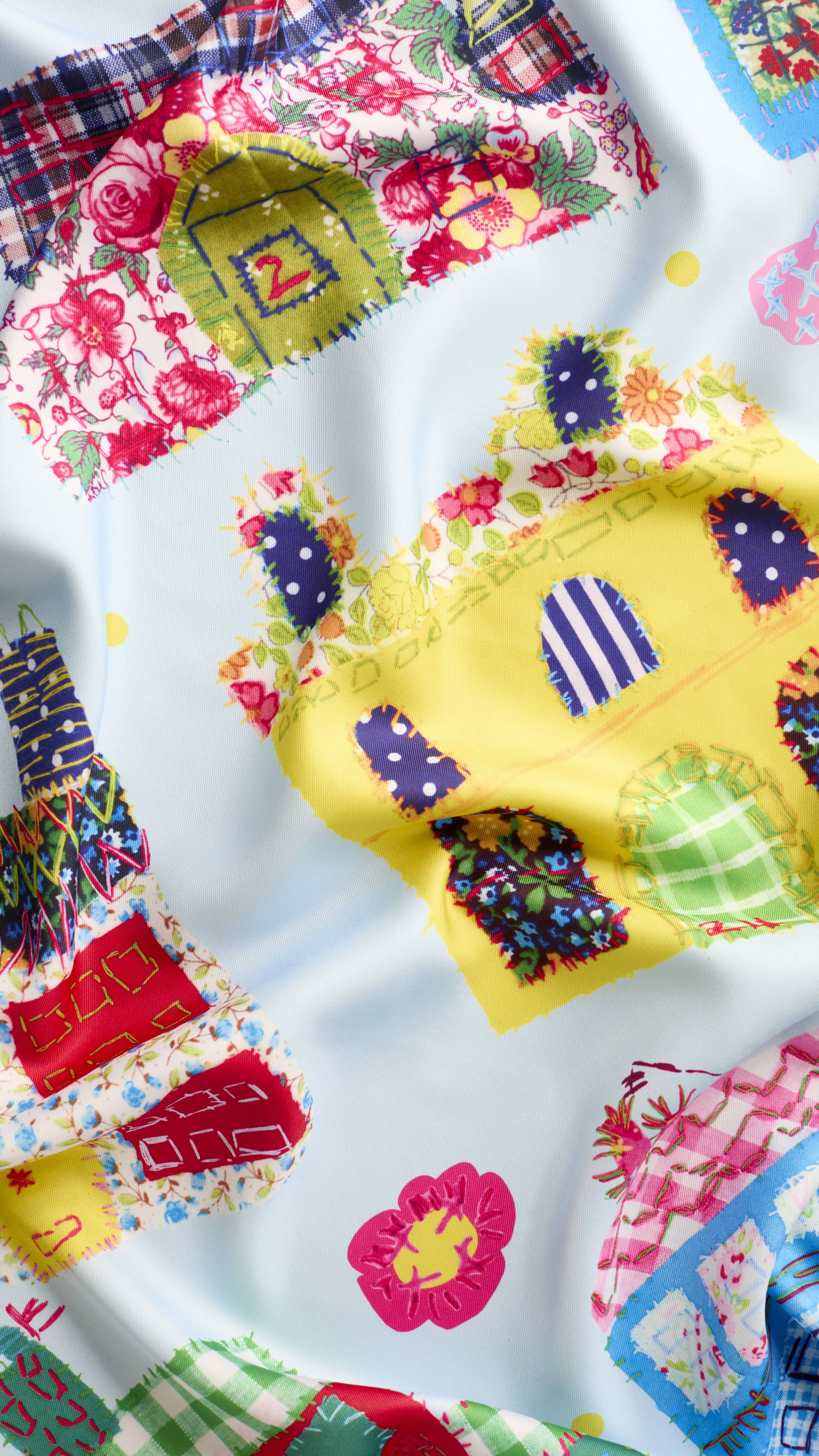 A super close-up texture shot of the "My Family Houses" fabric knot wrap. The image focuses on the soft texture of the knot wrap material and the vibrancy of the colours in the patchwork-style house design.