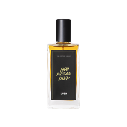 A glass perfume bottle filled with amber liquid. A black label reads 'The Perfume Library' and '1000 Kisses Deep'.