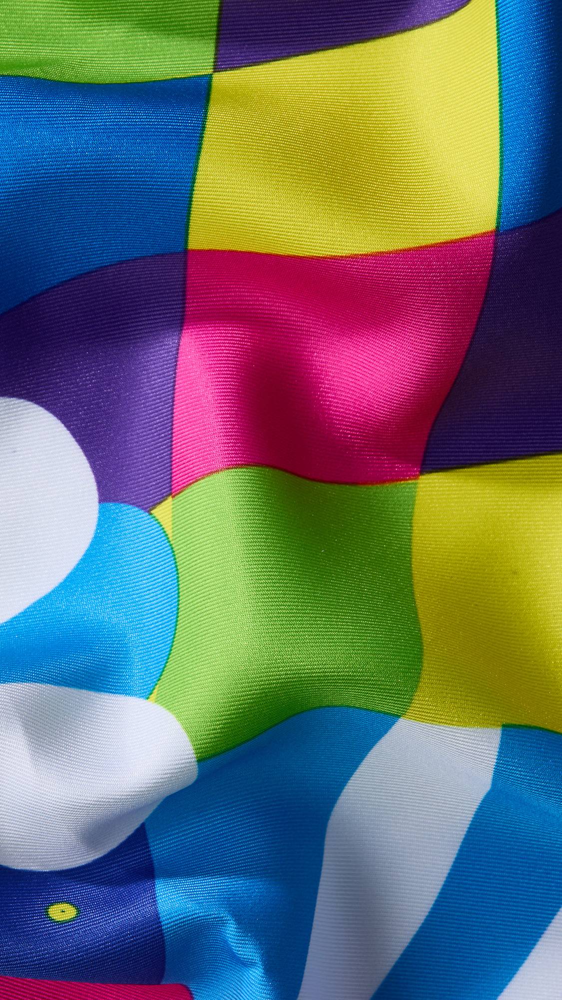 A super close-up image of the Gemini knot wrap to focus on the vibrant contrasting colours and the texture of the fabric. The area focused on has a checkered pattern of brightly coloured squares. 