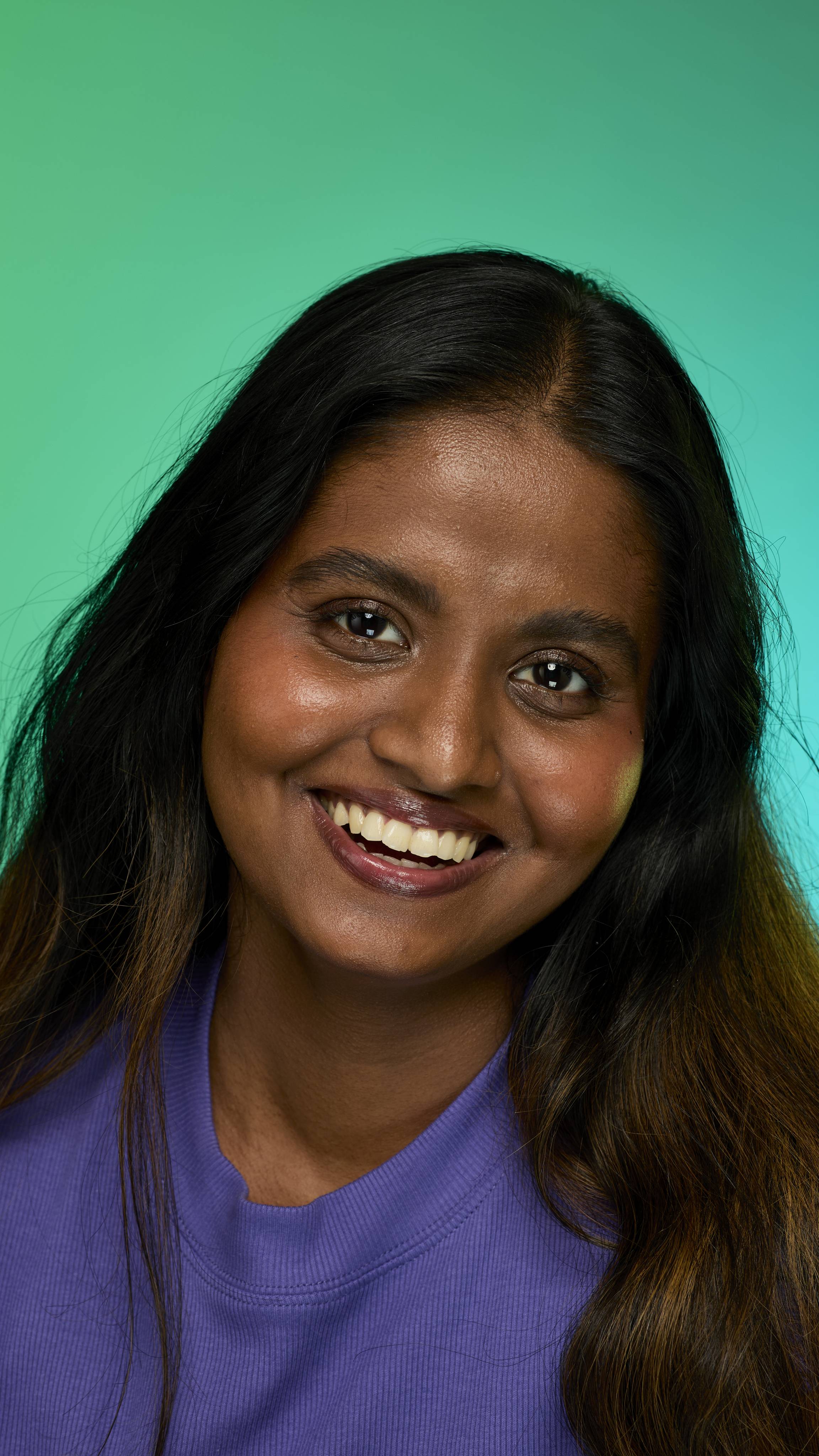 The image shows a model with dark straight hair on a green background. They are smiling at the camera as their eyebrows look thick and full thanks to the Noir brow pomade.