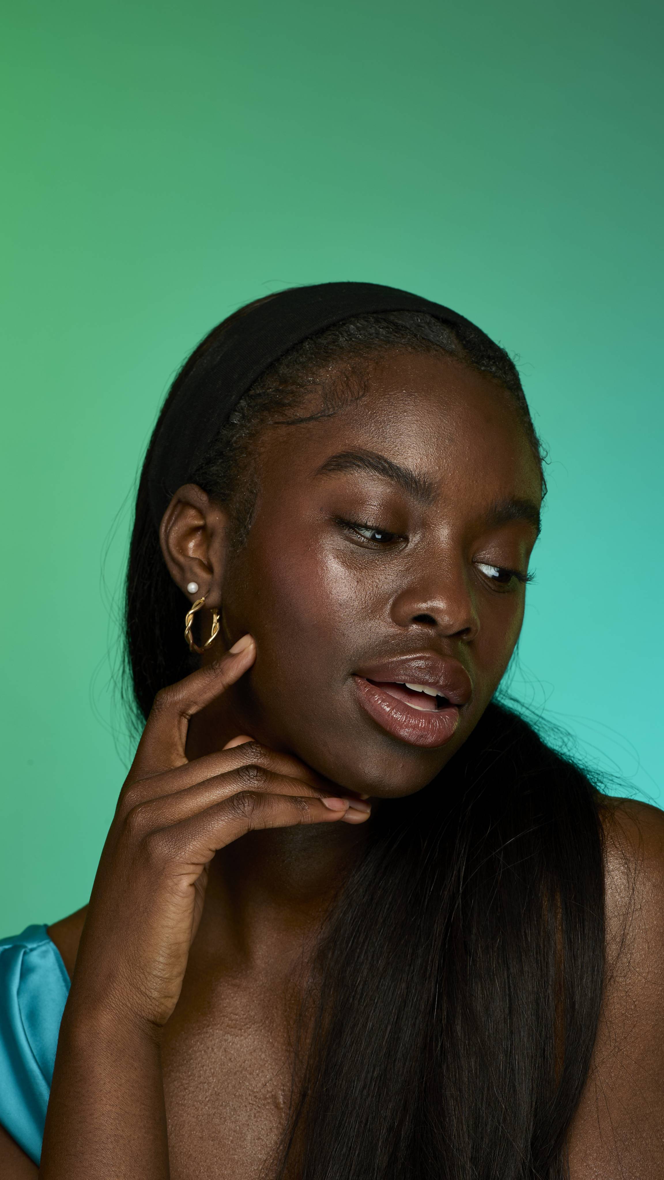 The image shows a model with dark straight hair on a green background. They are looking off-screen with their hand at their face as their eyebrows look thick and full thanks to the Smoke brow pomade.